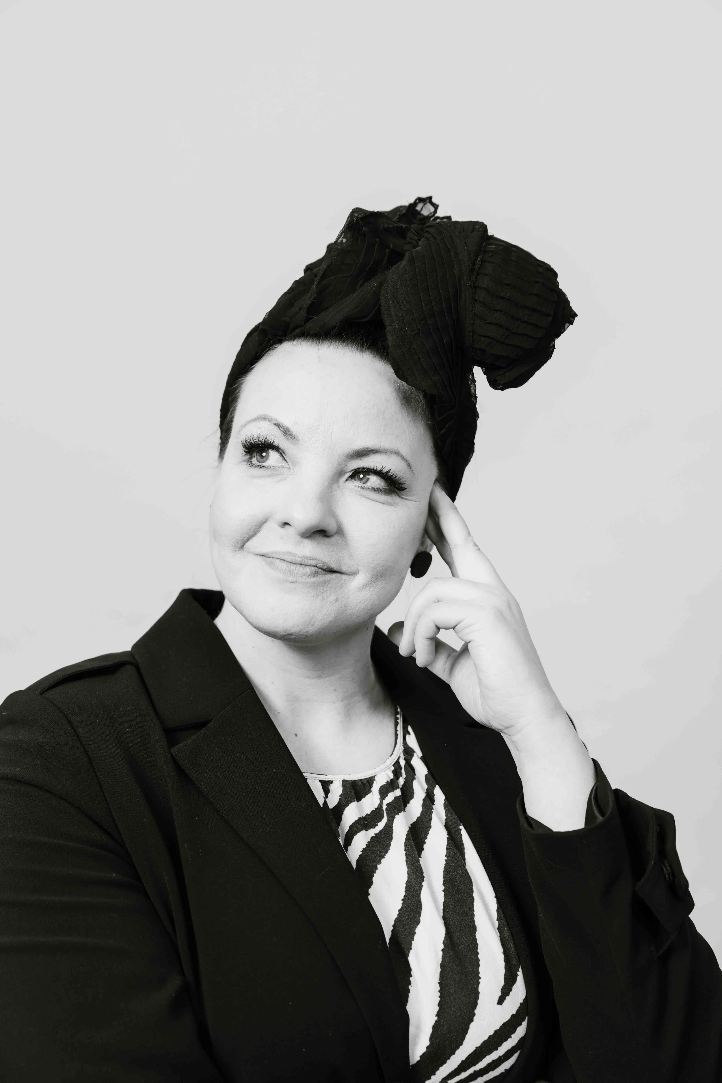 Nainen mustassa takissa ja zebraprinttisessä paidassa, päässään musta huivi, joka on sidottu korkealle, nainen hymyilee.