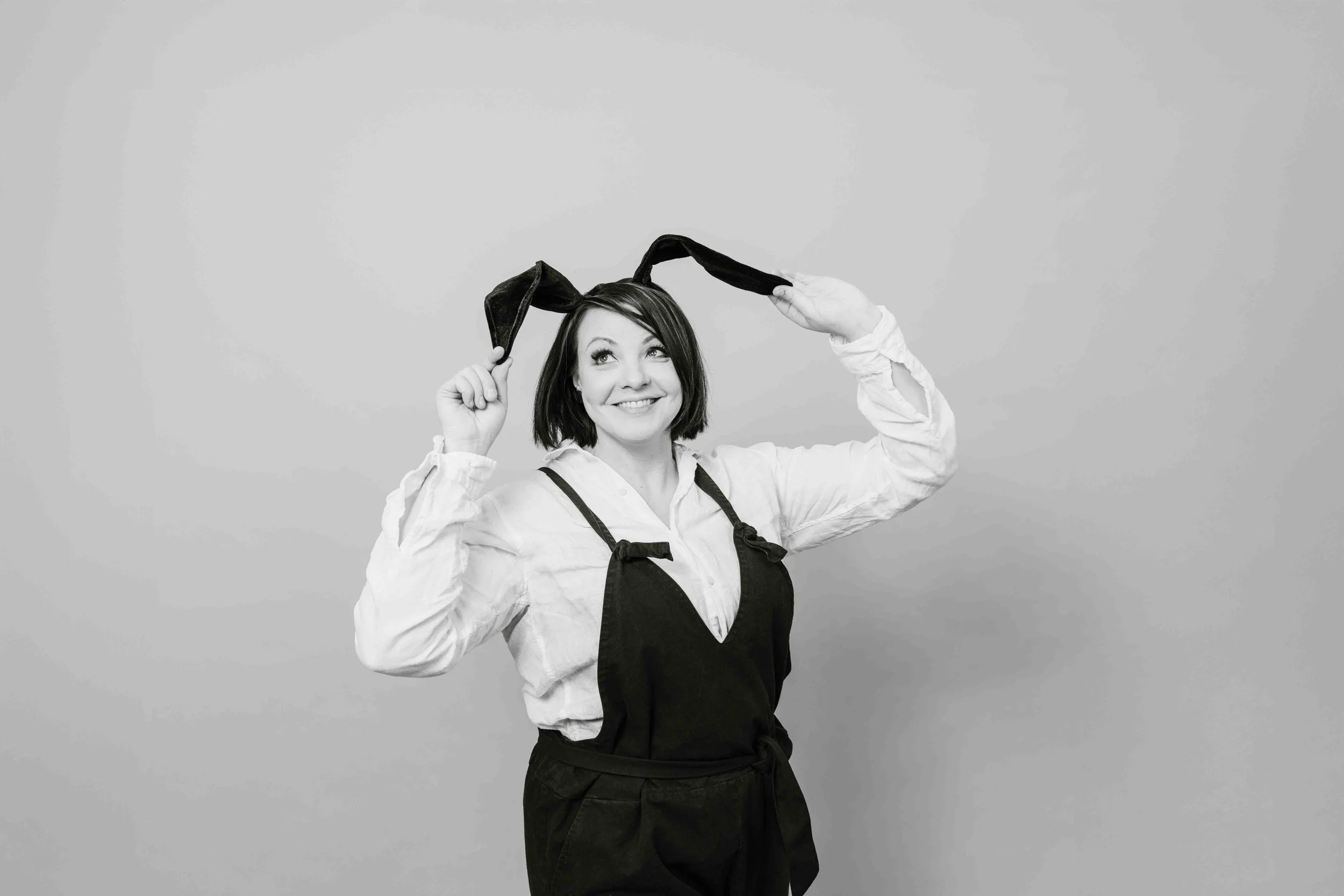 Nainen hymyilee ja pitää käsillä kiinni hiuspannasta, jossa on pitkät korvat.