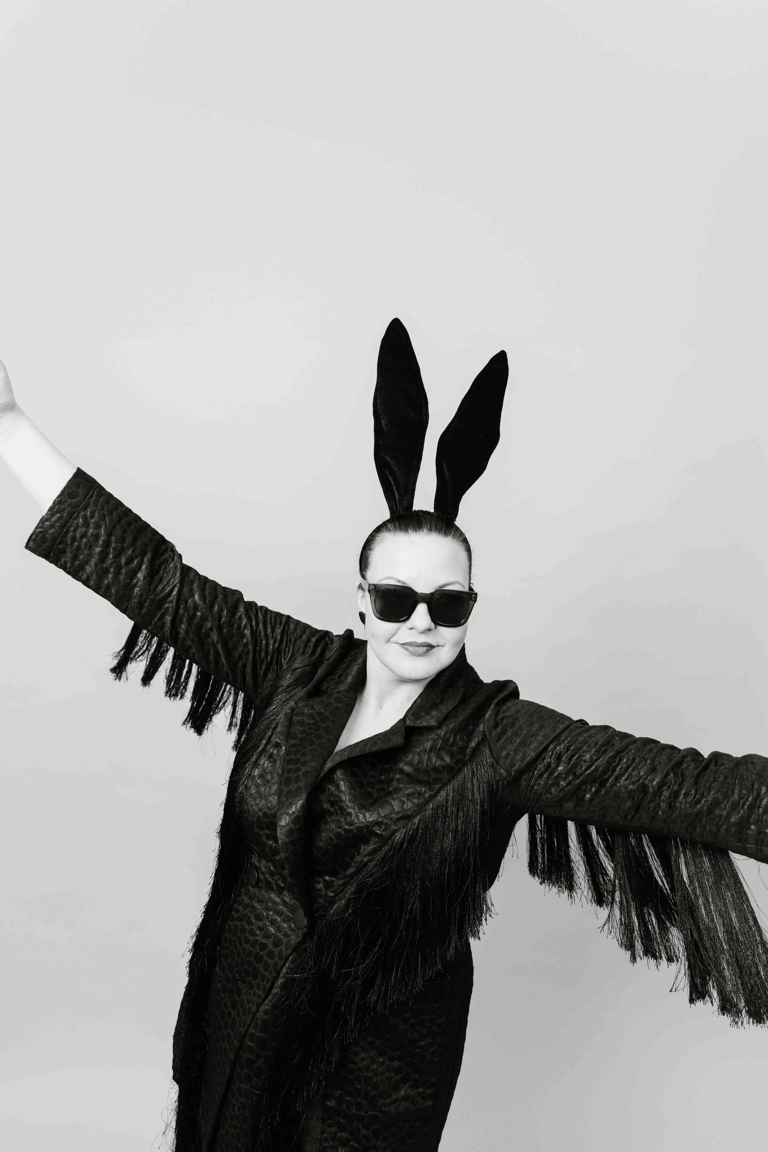 Nainen, jolla on musta hapsuhihainen nahkatakki, suuret aurinkolasit ja pupunkorvat.