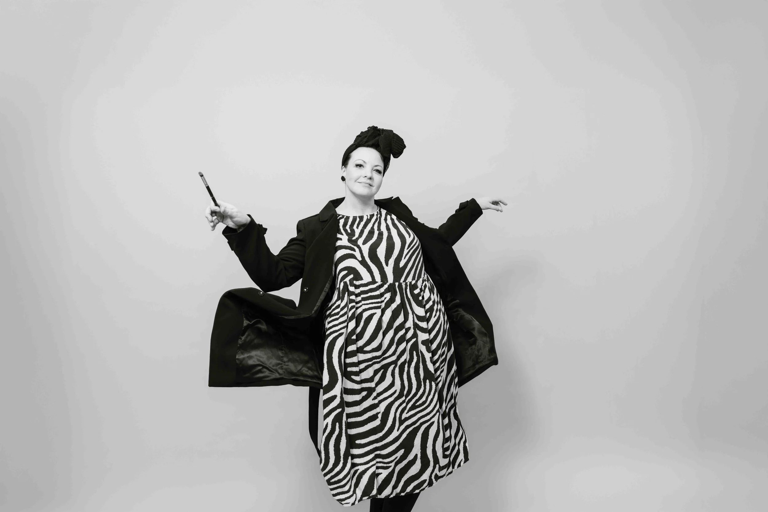 Hymyilevä nainen eläinkuviollinen mekko päällä, taikasauva kädessään.