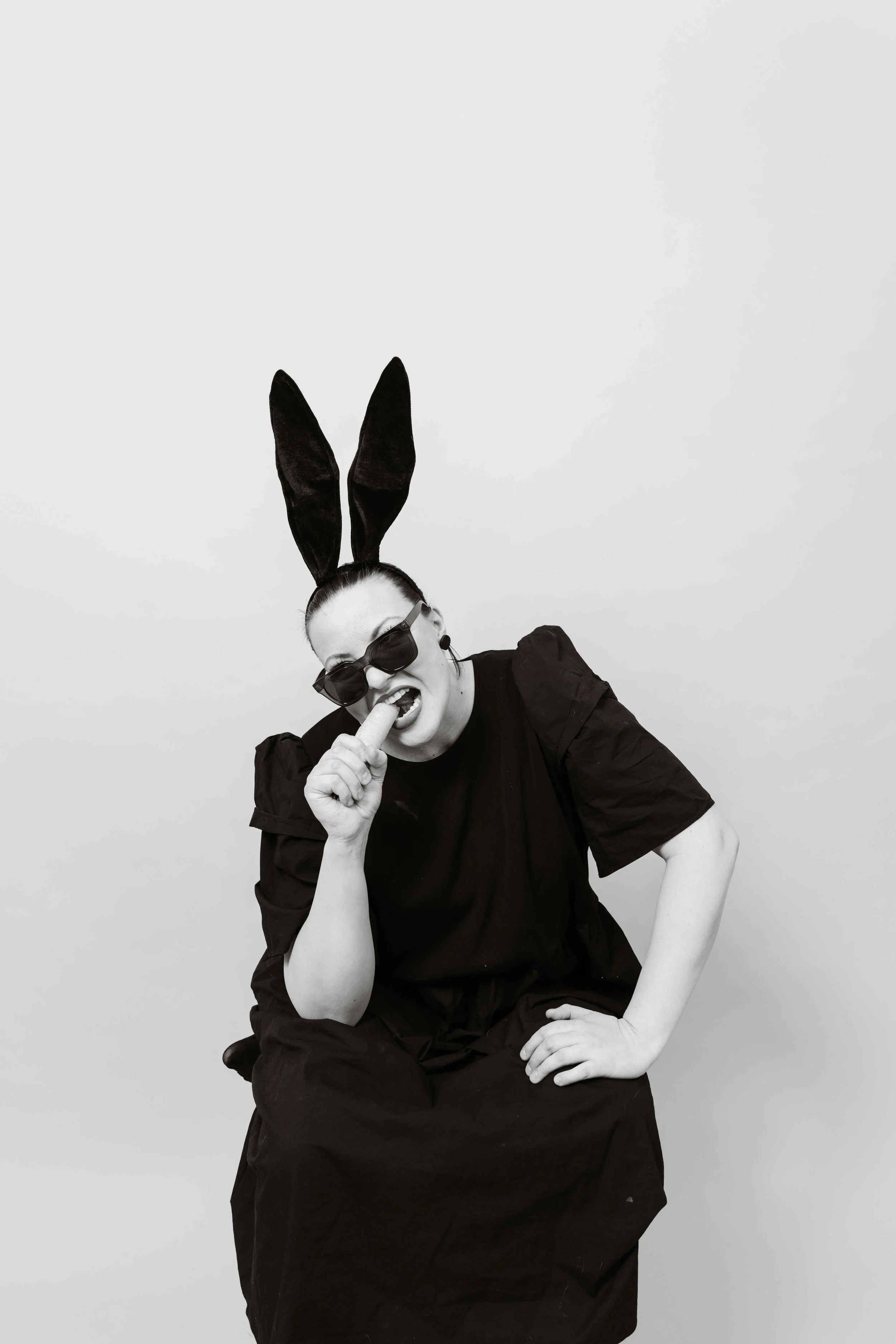 Nainen on pukeutunut mustaan, hänellä on suuret mustat pupunkorvat, mustat aurinkolasit ja huumorintajuinen ilme.