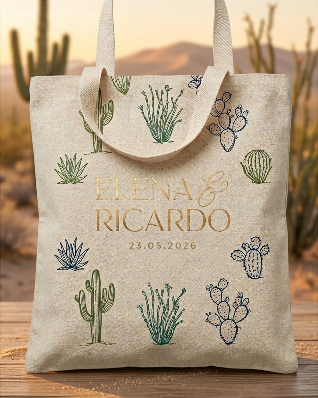 Bolsa de tela beige con dibujos de cactus y plantas en colores verde y azul, con nombres en dorado y en color caqui, con la fecha 23.05.2026 en letras pequeñas.