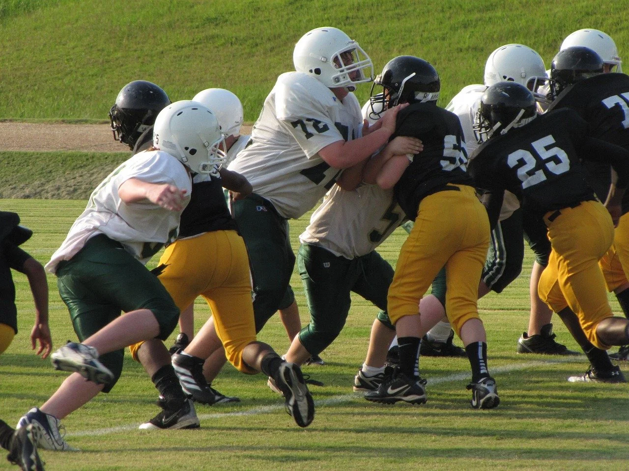 Youth football game with players in white and black uniforms engaging at the line of scrimmage on a grass field.