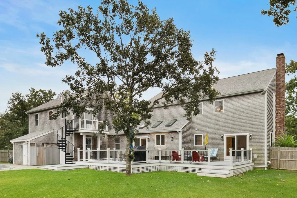 Backyard of a house with a large tree, a deck with outdoor furniture, and a fenced yard.