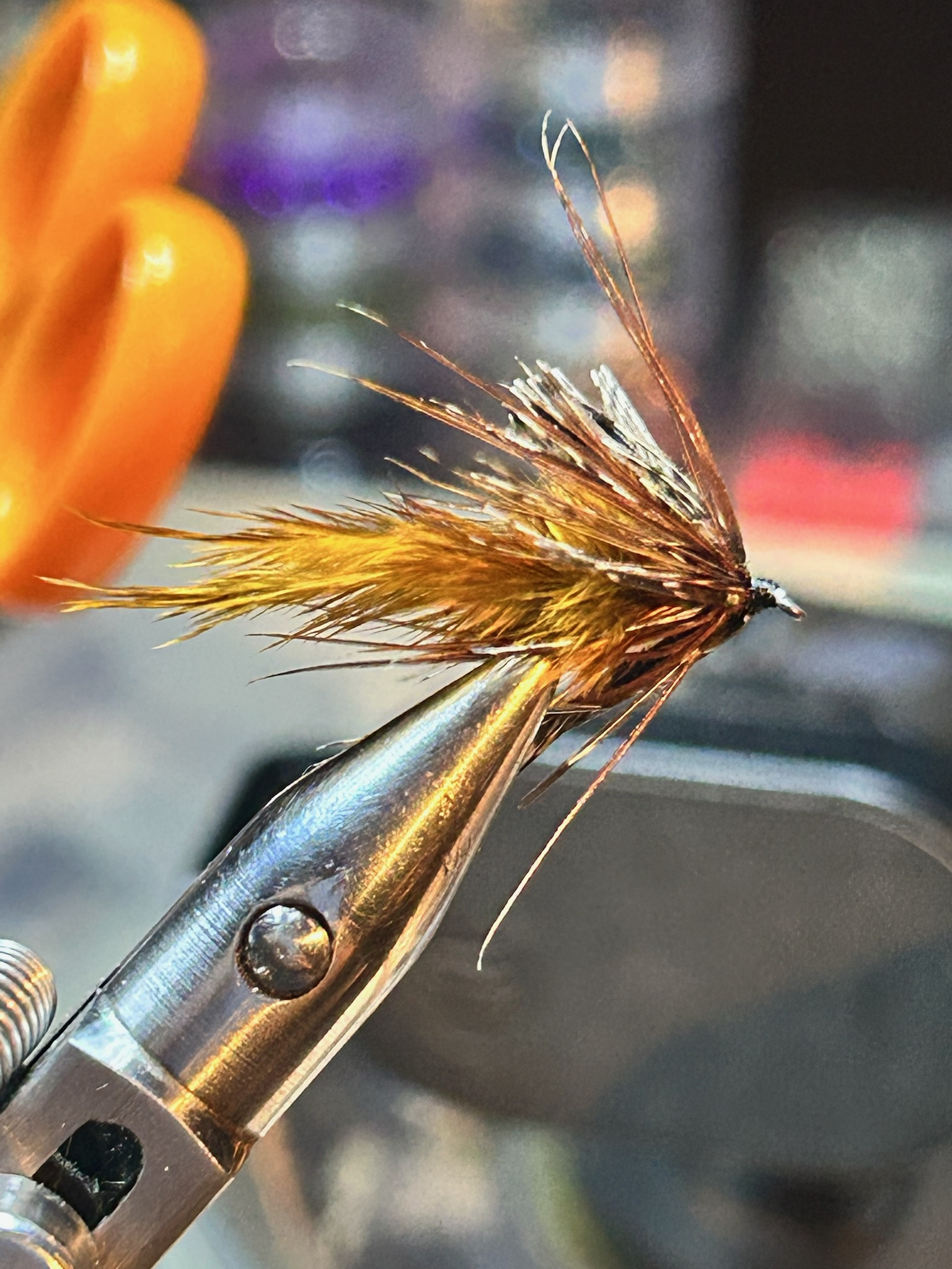 Close-up of a fishing fly with brown and yellow feathers held in a metallic fishing hook.