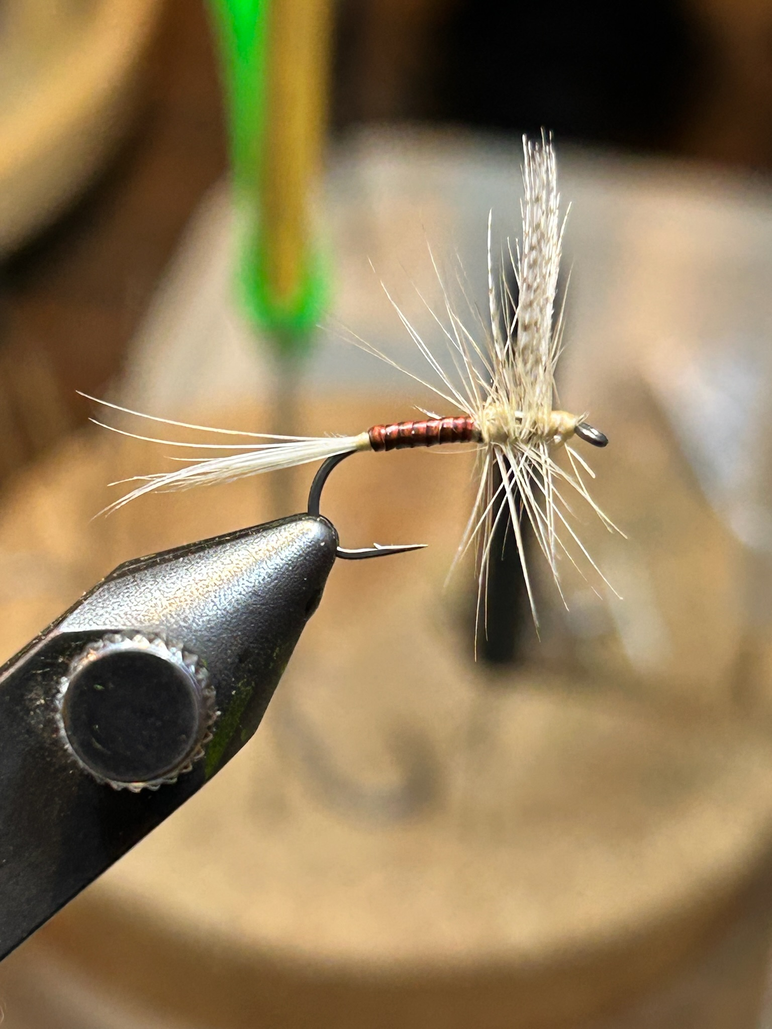 Close-up of a fishing fly tied on a hook, used for fly fishing, with a blurred background.