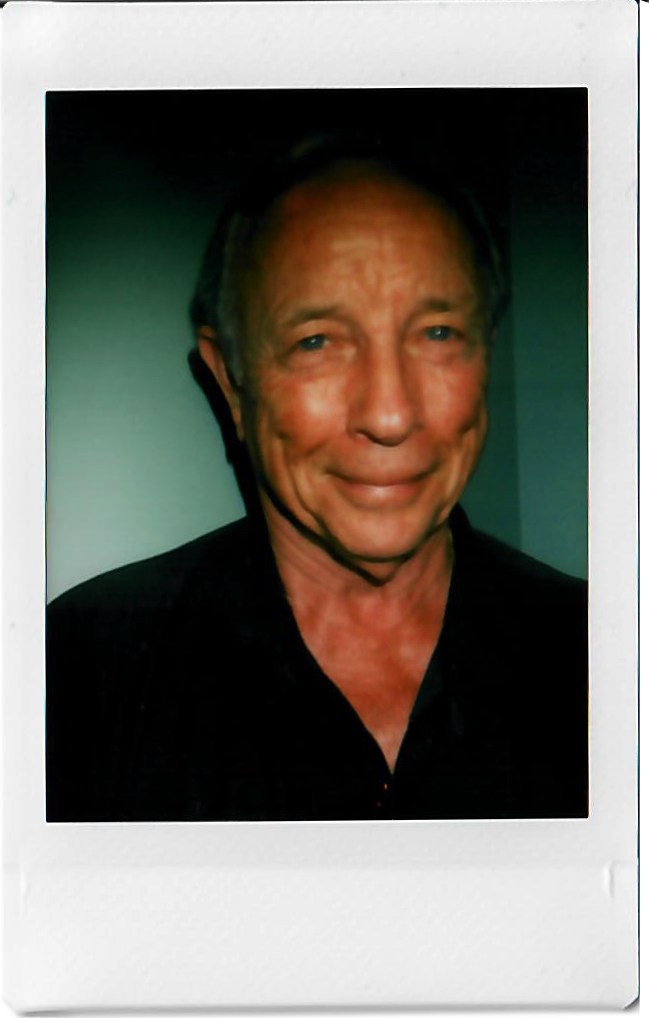 A man with a warm smile, wearing a dark shirt, against a dark background.