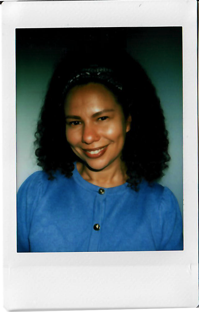 A woman with dark curly hair, wearing a blue top and smiling in a portrait photograph.