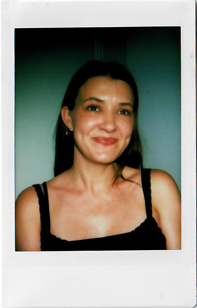 A woman with dark hair wearing a black tank top, smiling in front of a dark background.