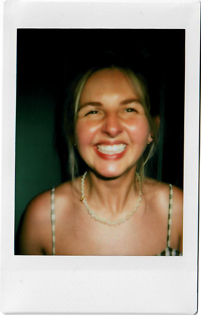 Smiling woman with blonde hair, wearing a necklace and spaghetti strap top, in a Polaroid photo.
