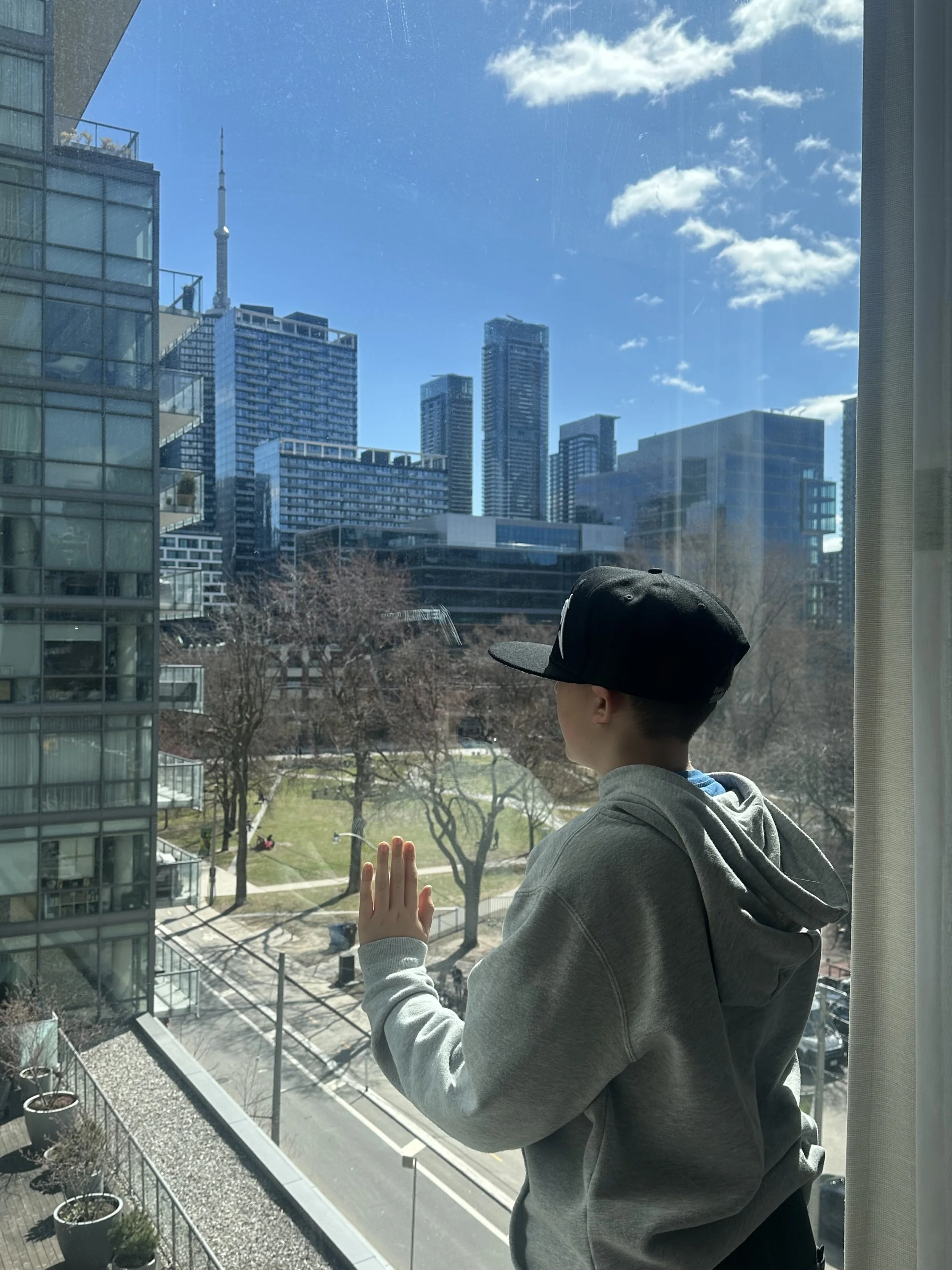 A young person looks out over Toronto's skyline, hand against the glass. The future ahead.