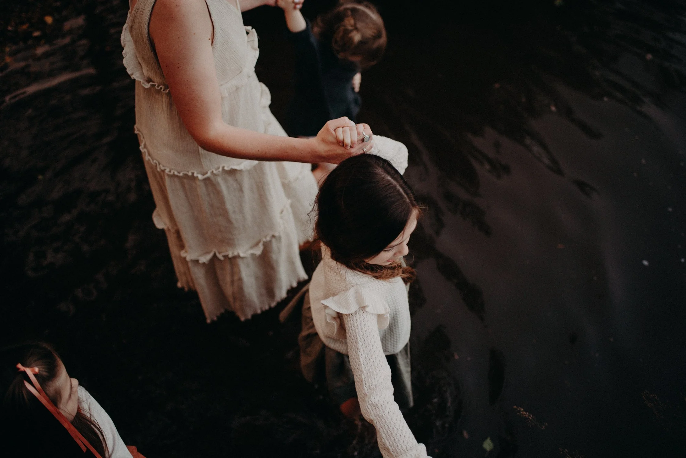 A woman and children stand in water, with only their upper bodies visible, and their heads bowed.