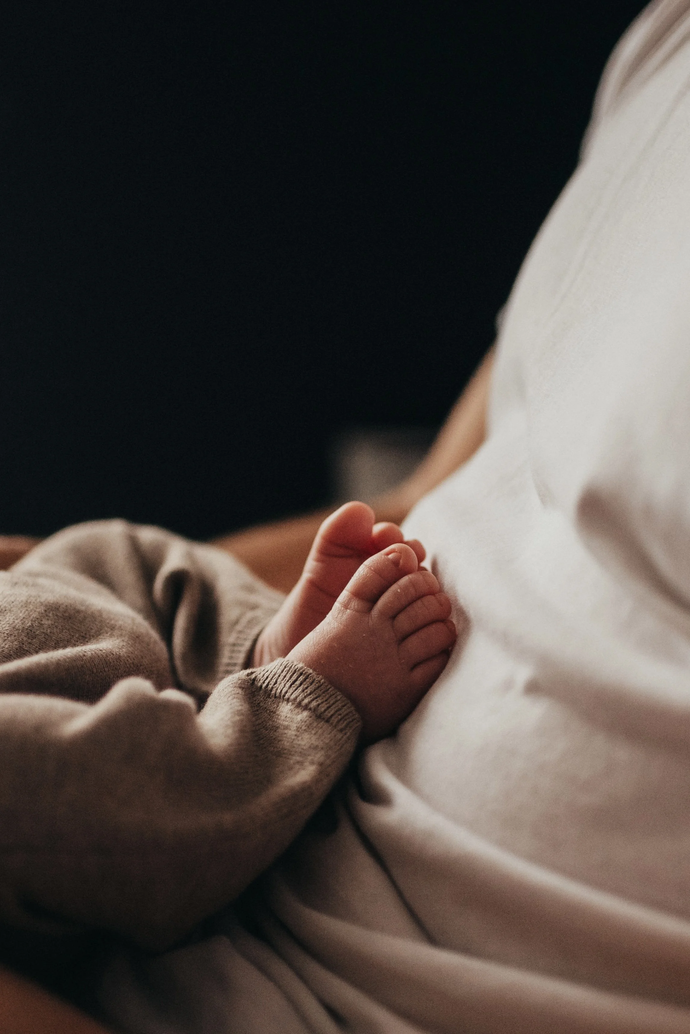 Close-up of a baby's hand resting on an adult's chest, with warm lighting and soft clothing.