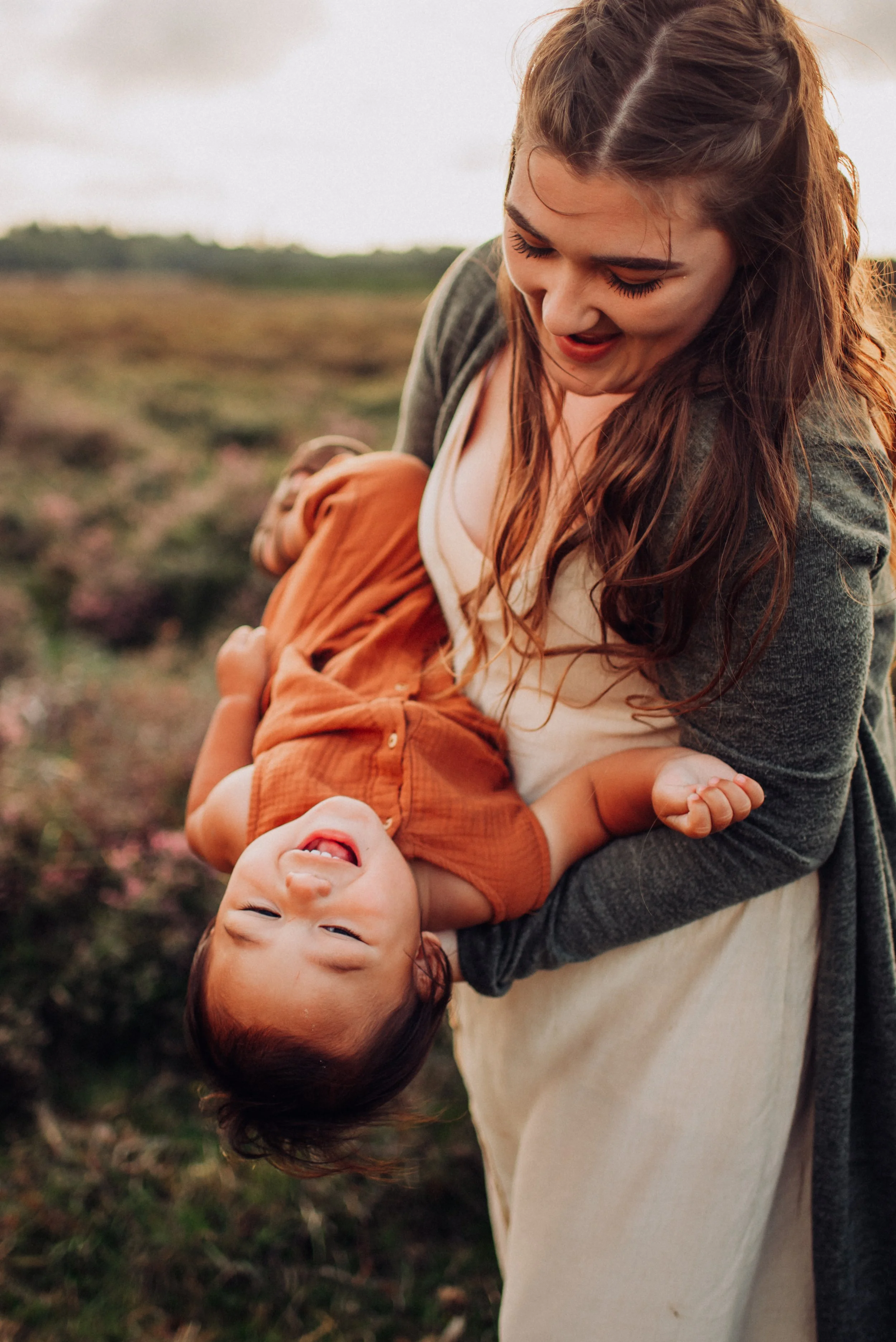 A woman holding a laughing young boy in a field with pink flowers, evening light.