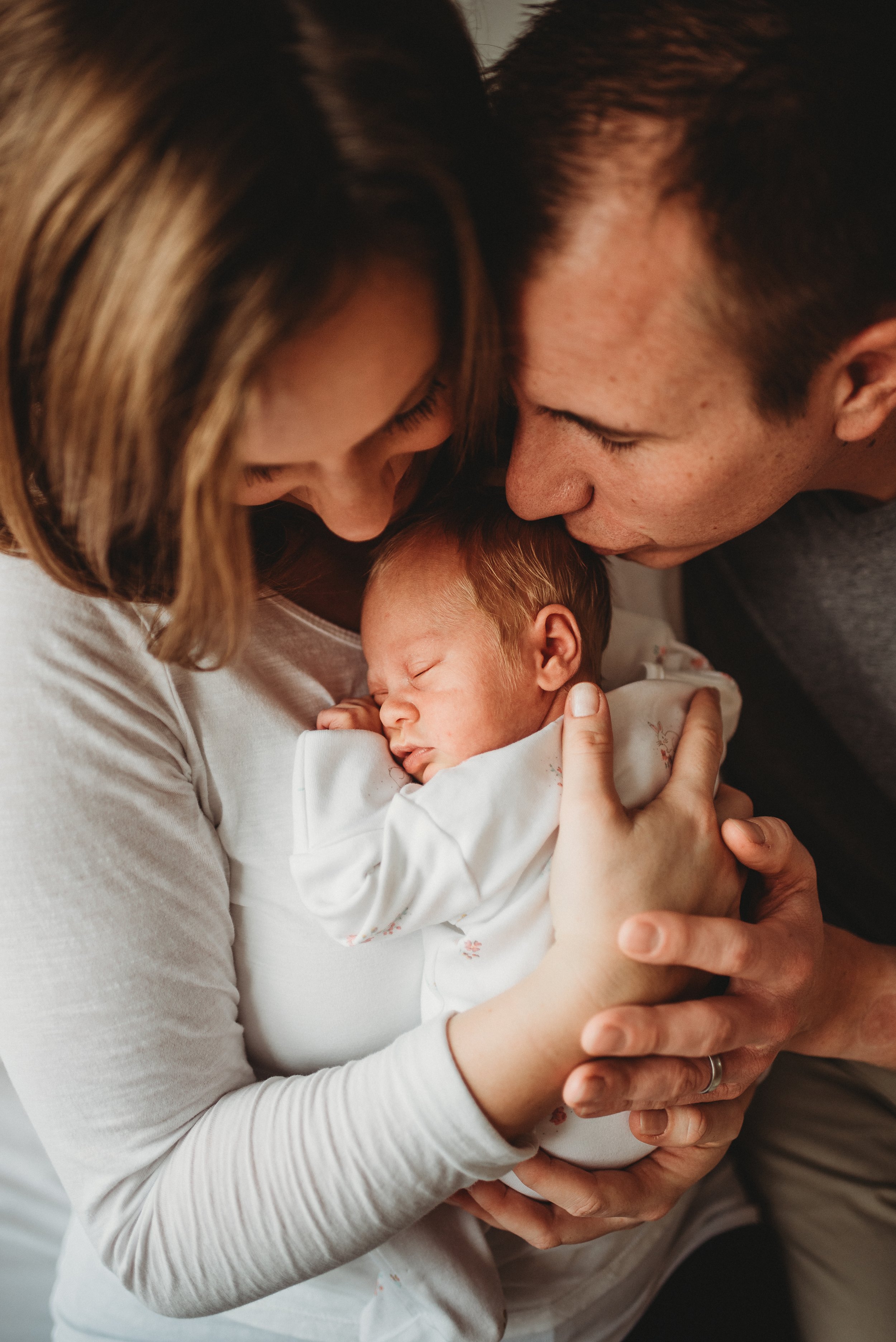 A woman and a man closely holding a sleeping newborn baby, touching their foreheads together.
