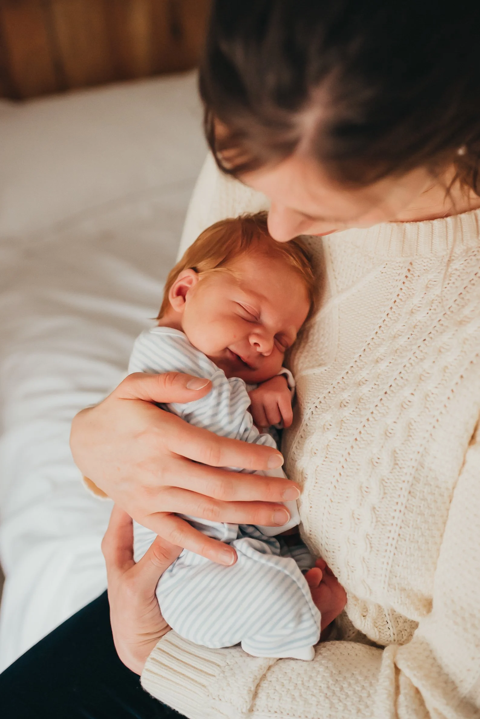 A woman holding a smiling sleeping newborn baby close to her chest indoors.