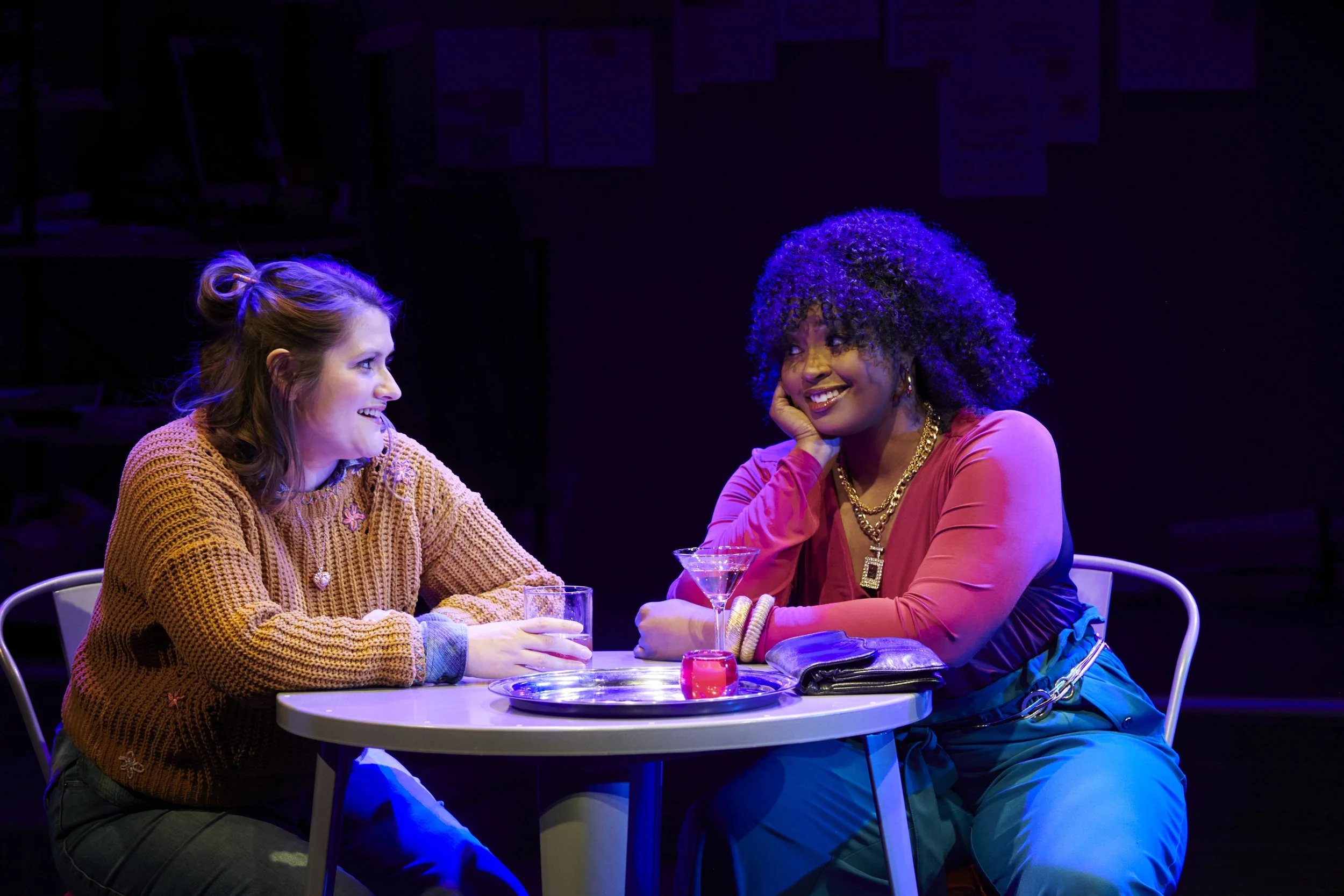 Two women look at each other, laughing, over drinks.
