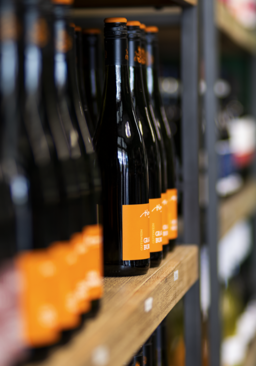 Bierflaschen mit orangefarbenem Etikett auf einer Holzregal im Supermarkt.