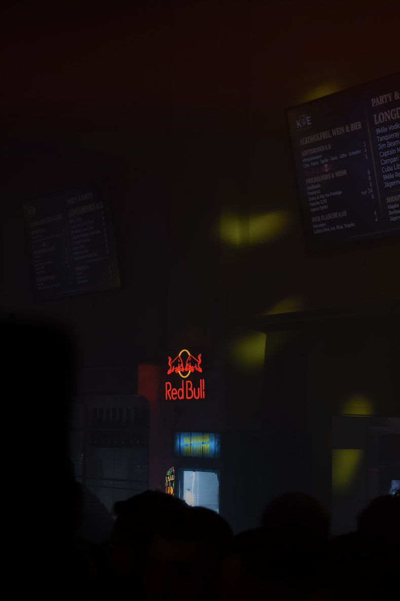 Leuchtreklame von Red Bull in einer dunklen Bar oder Club, mit anderen Anzeigetafeln im Hintergrund.