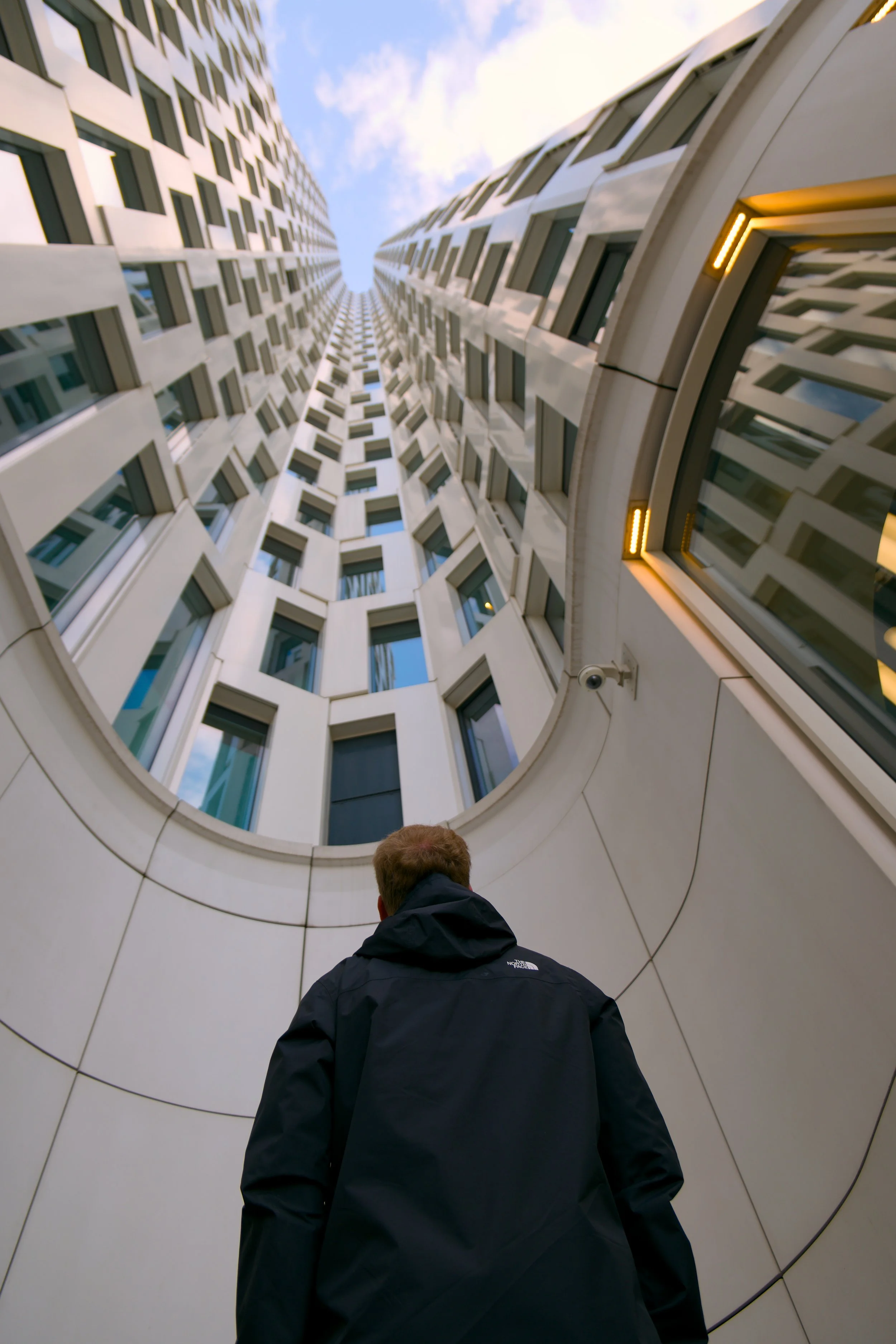 Ein Mann steht vor einem hohen modernen Gebäude mit vielen Fenstern, der Blick ist nach oben gerichtet, Blick nach oben auf die Fassade des Gebäudes.