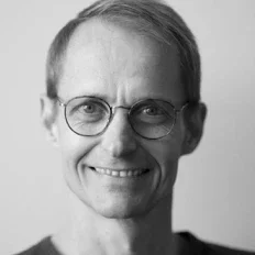 Schwarz-weiß-Porträt eines Mannes mit kurzen Haaren, Brille und freundlichem Lächeln.