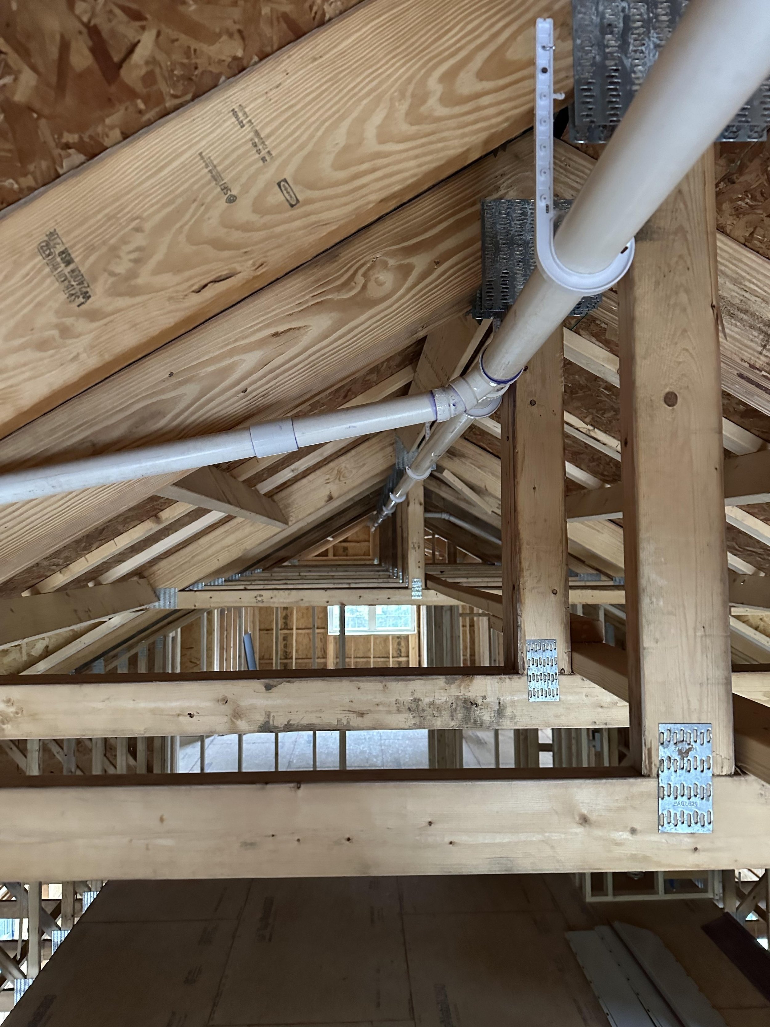Interior view of the attic framing with wooden beams, electrical conduit, and metal brackets.