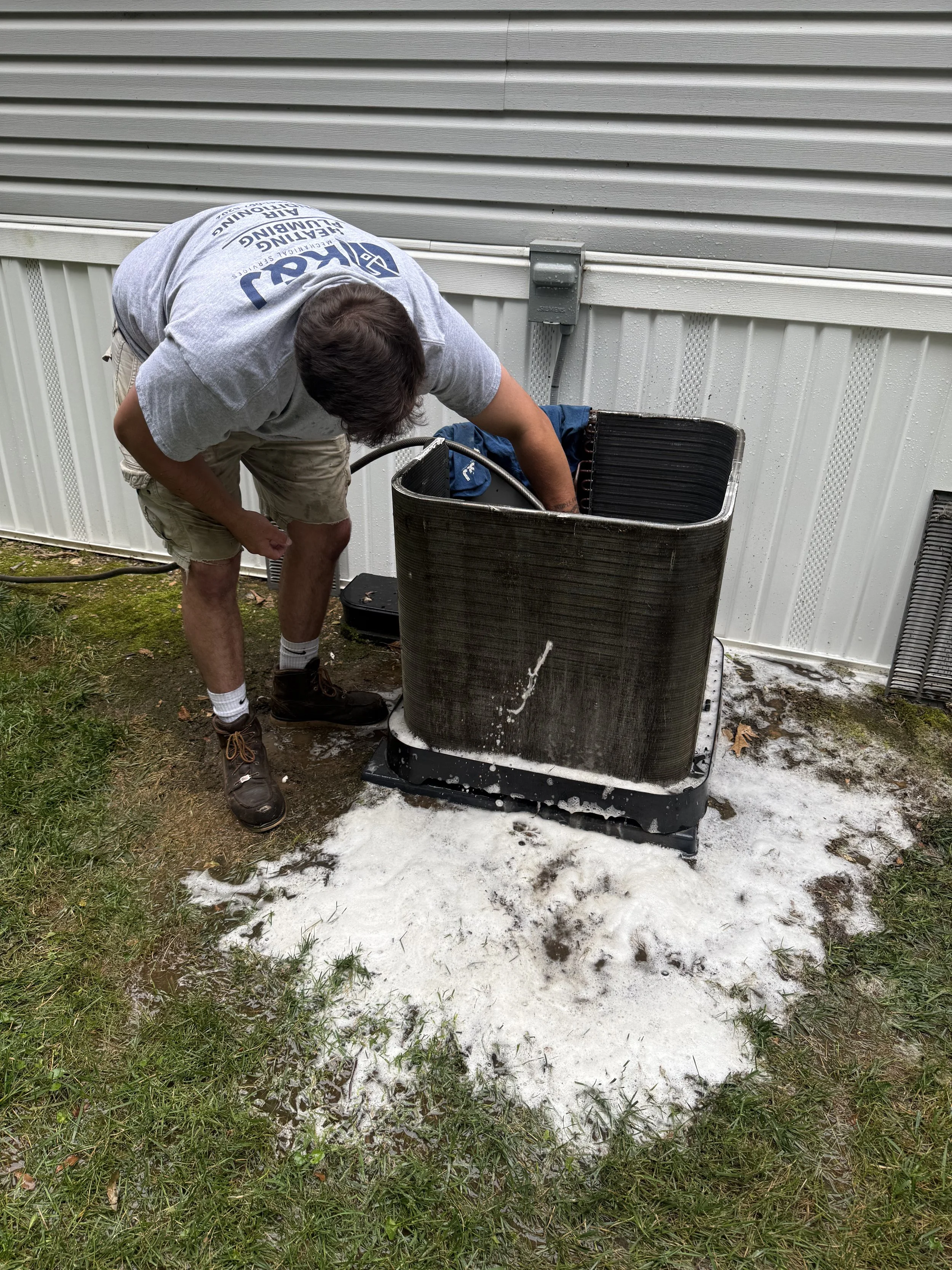 A person cleaning an outdoor air conditioning unit with soap and water.