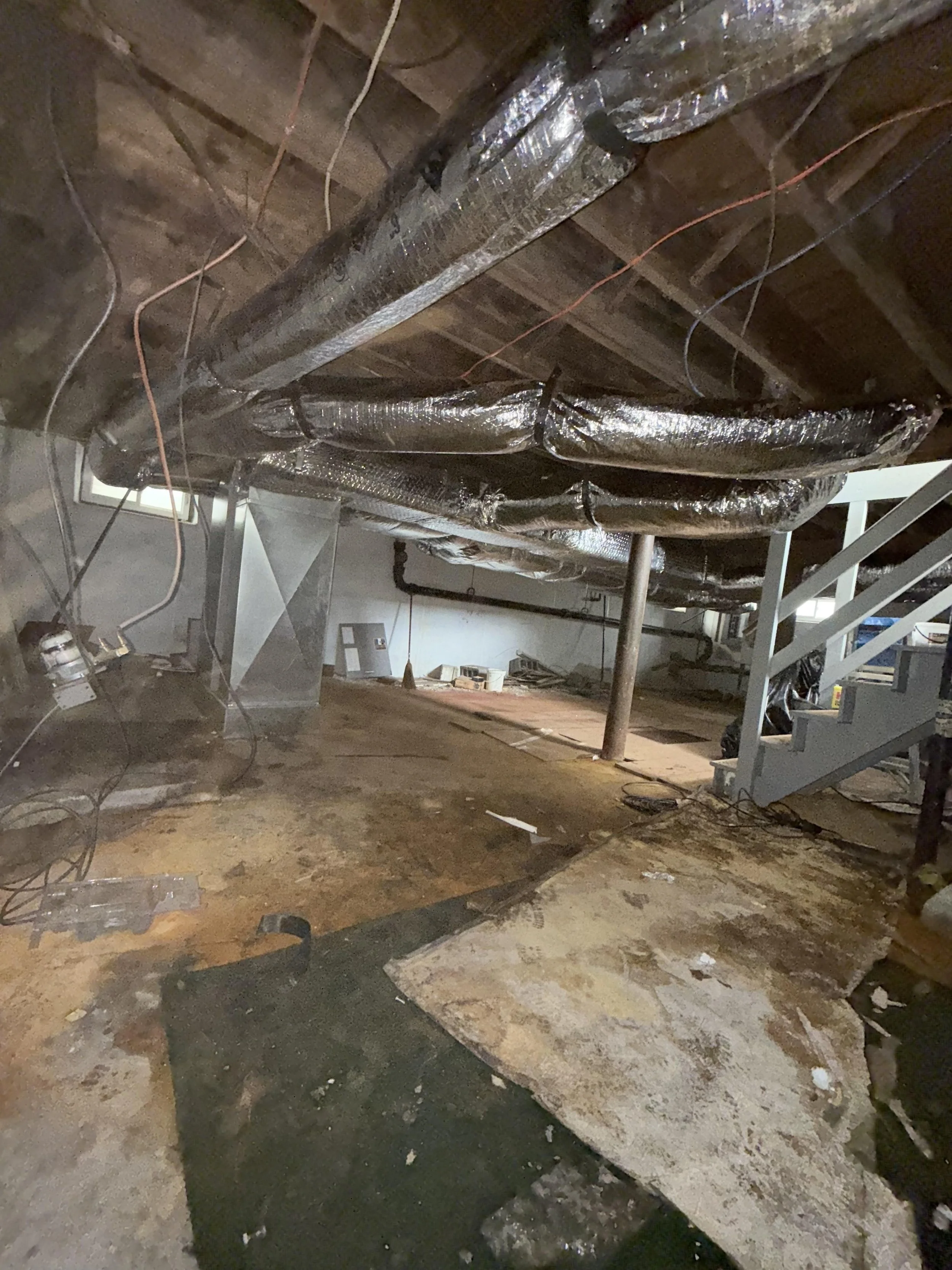 View of an unfinished basement or crawl space with exposed insulation, ductwork, and electrical wiring hanging from the ceiling, along with some construction equipment on the floor.