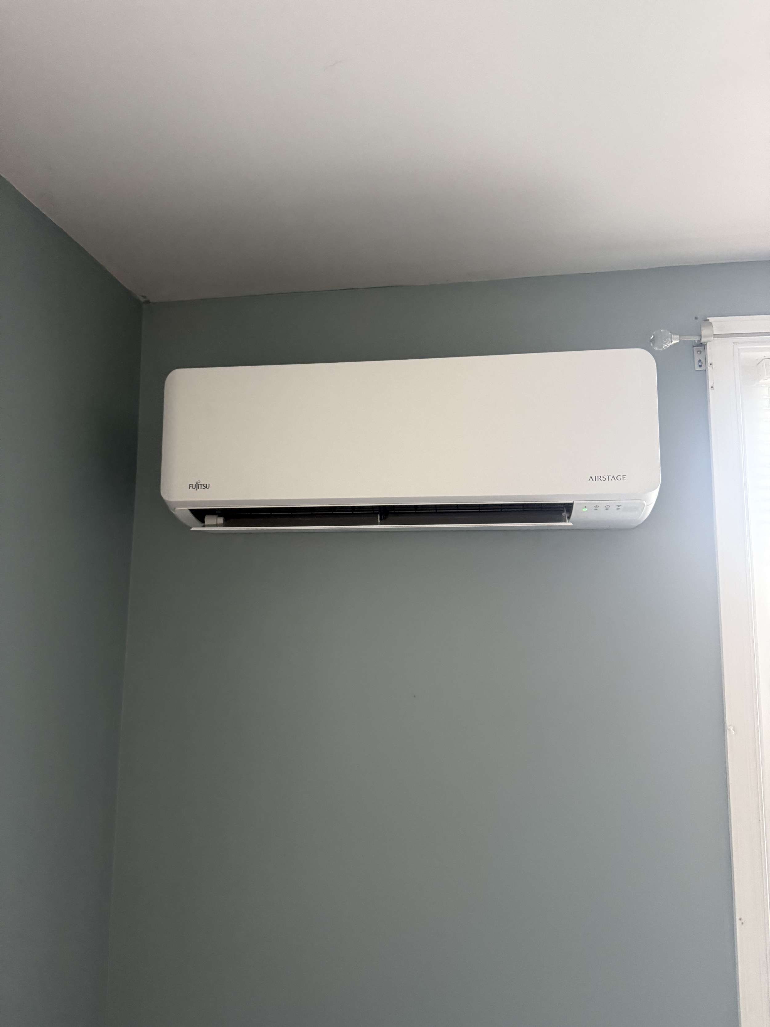 Wall-mounted Fujitsu AirStage air conditioning unit on a light gray wall in a room.