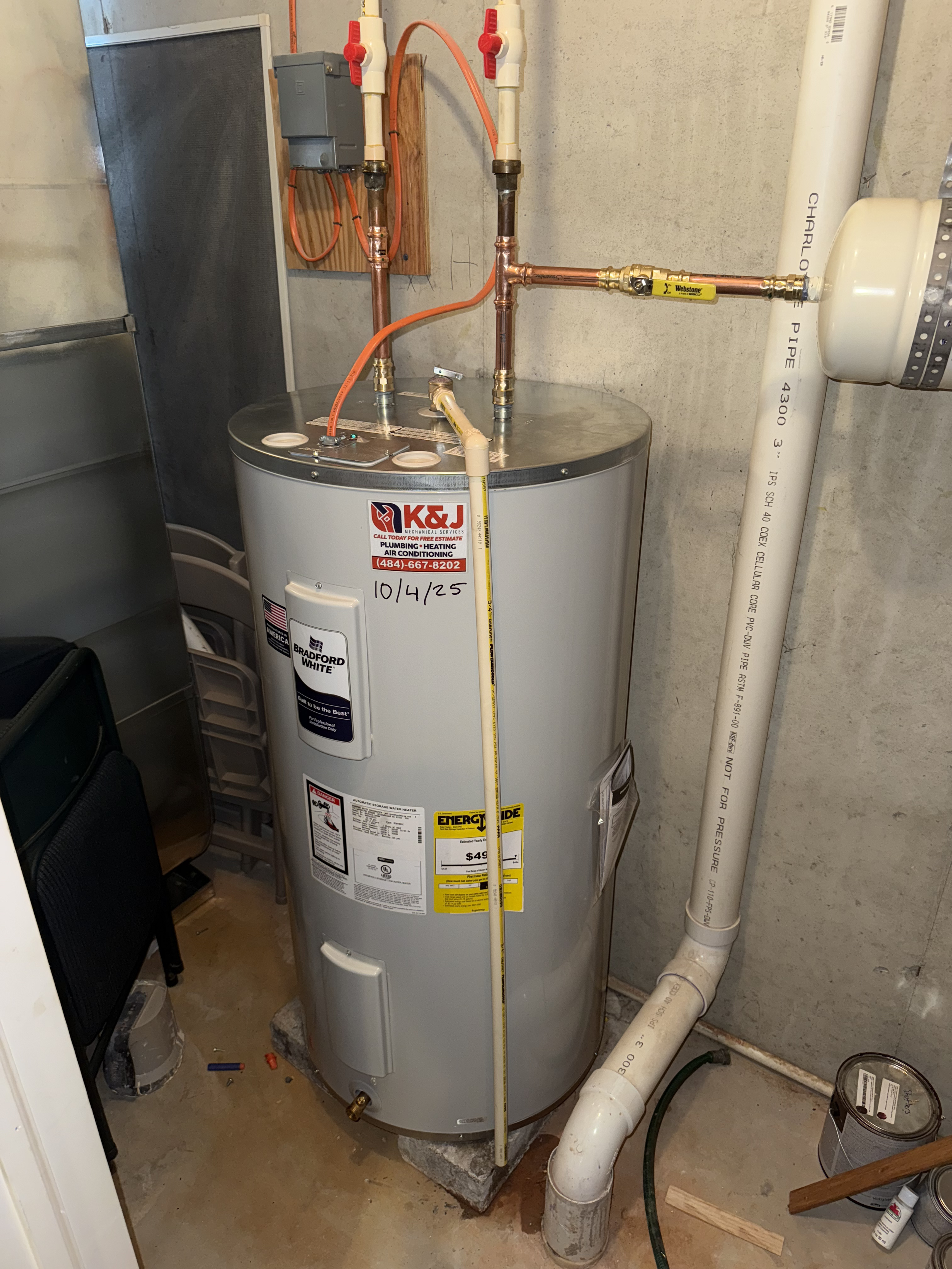 A water heater installed in a basement with plumbing pipes connected to it and some labels on the front.