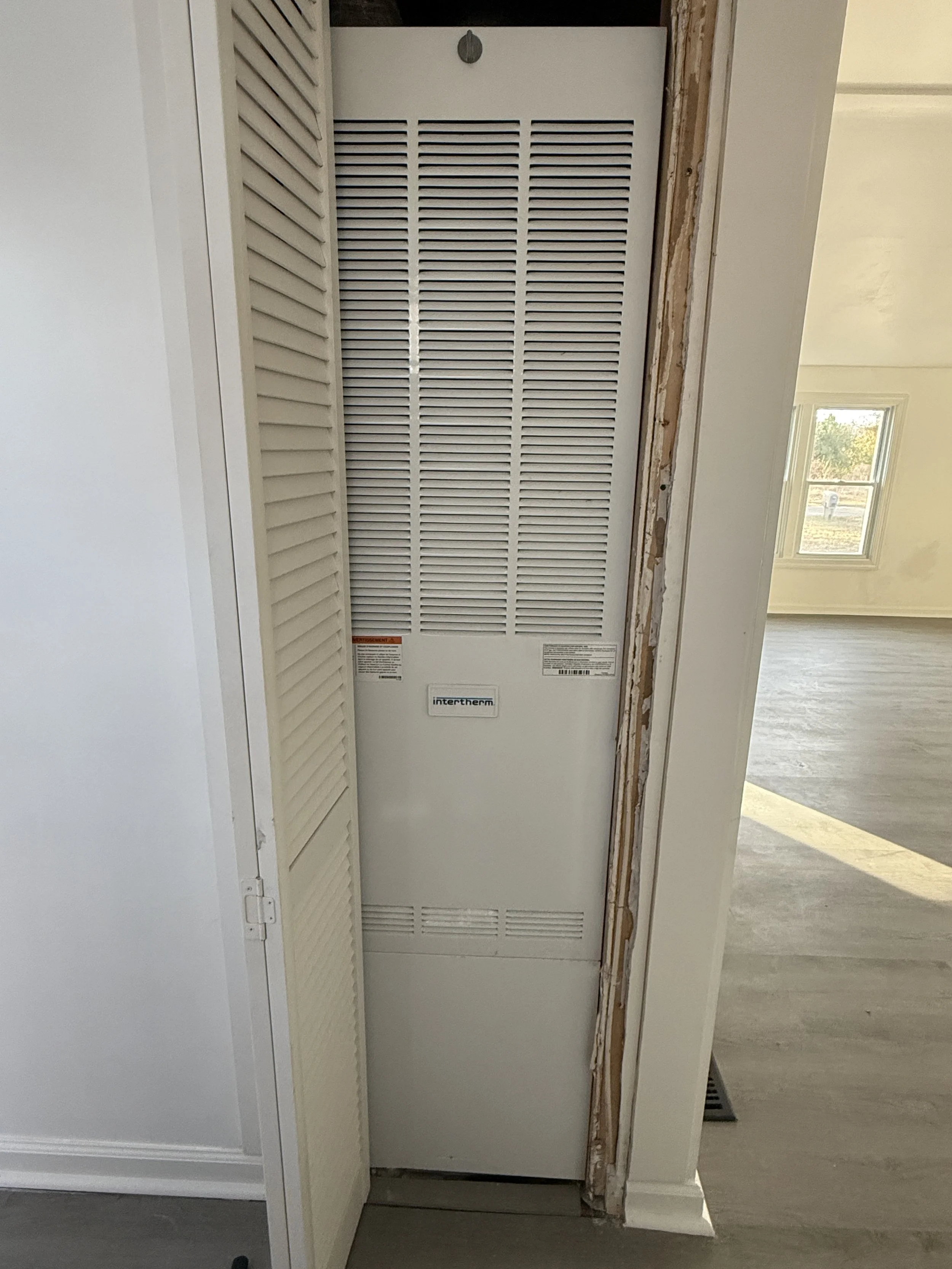 View of HVAC system or furnace behind a partially open closet door in a room with light-colored walls and wooden flooring.