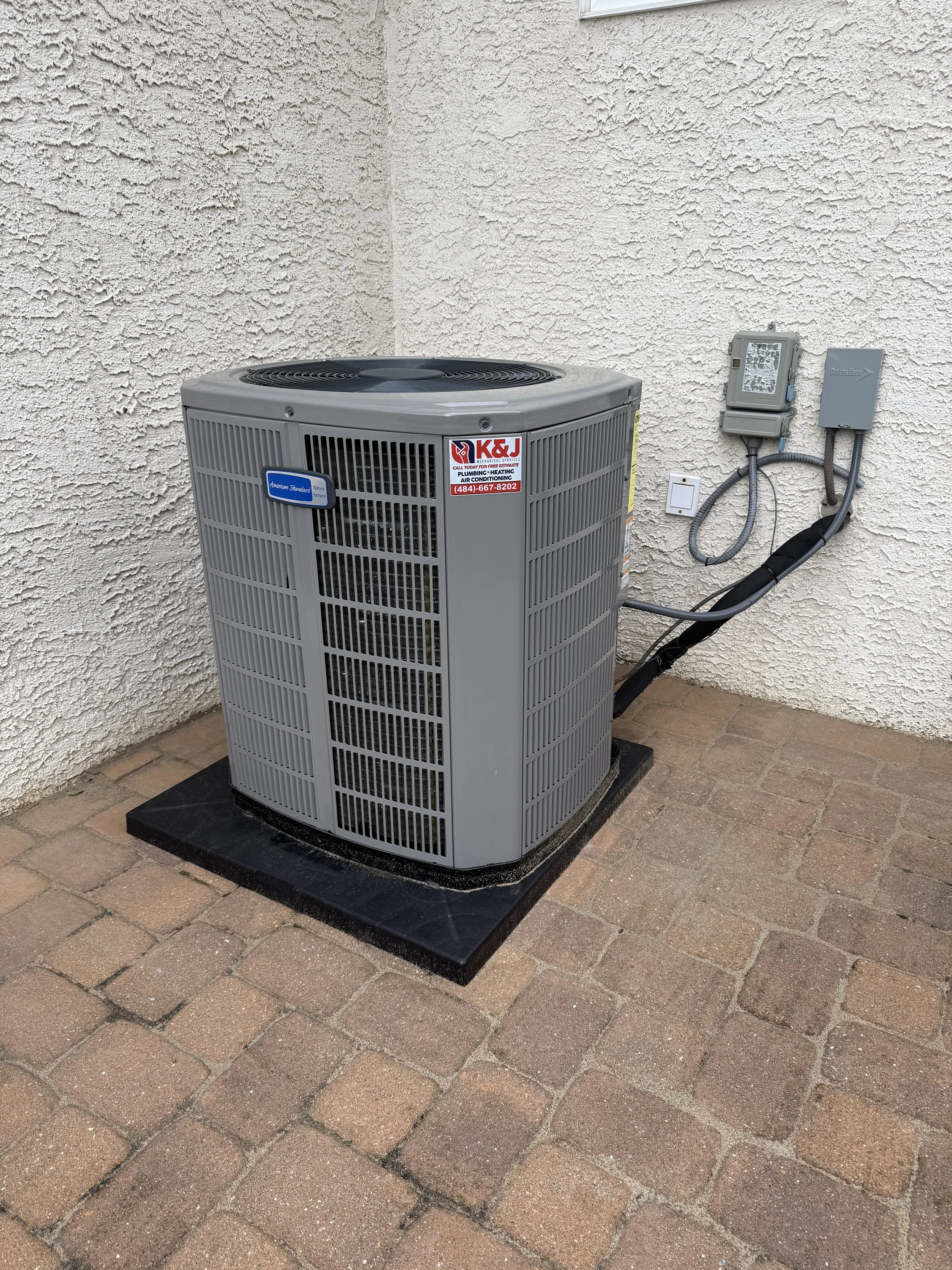 Outside air conditioning unit on a brick patio next to a textured cream-colored wall.