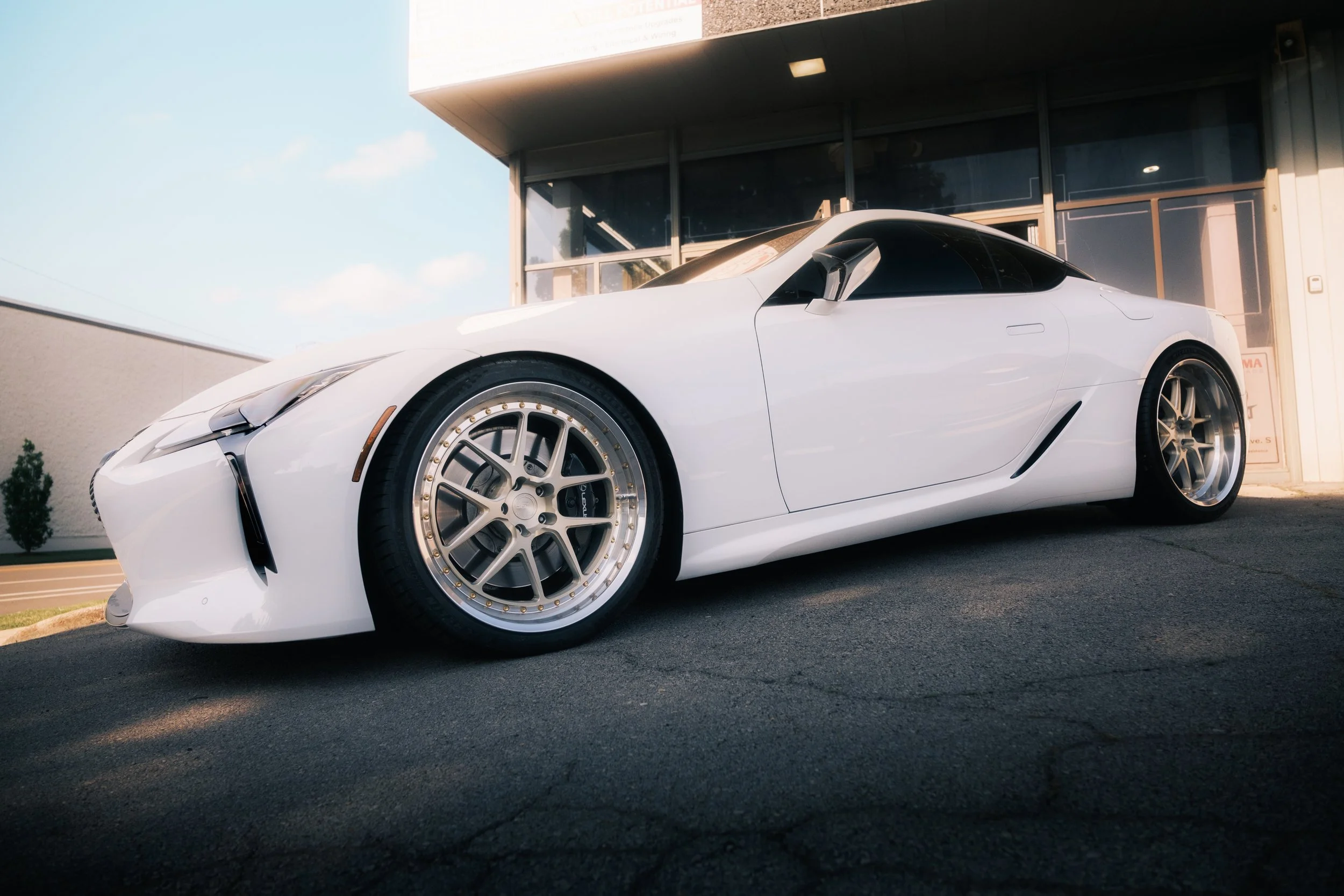 A white sports car parked outside a building with large glass windows and a modern design.