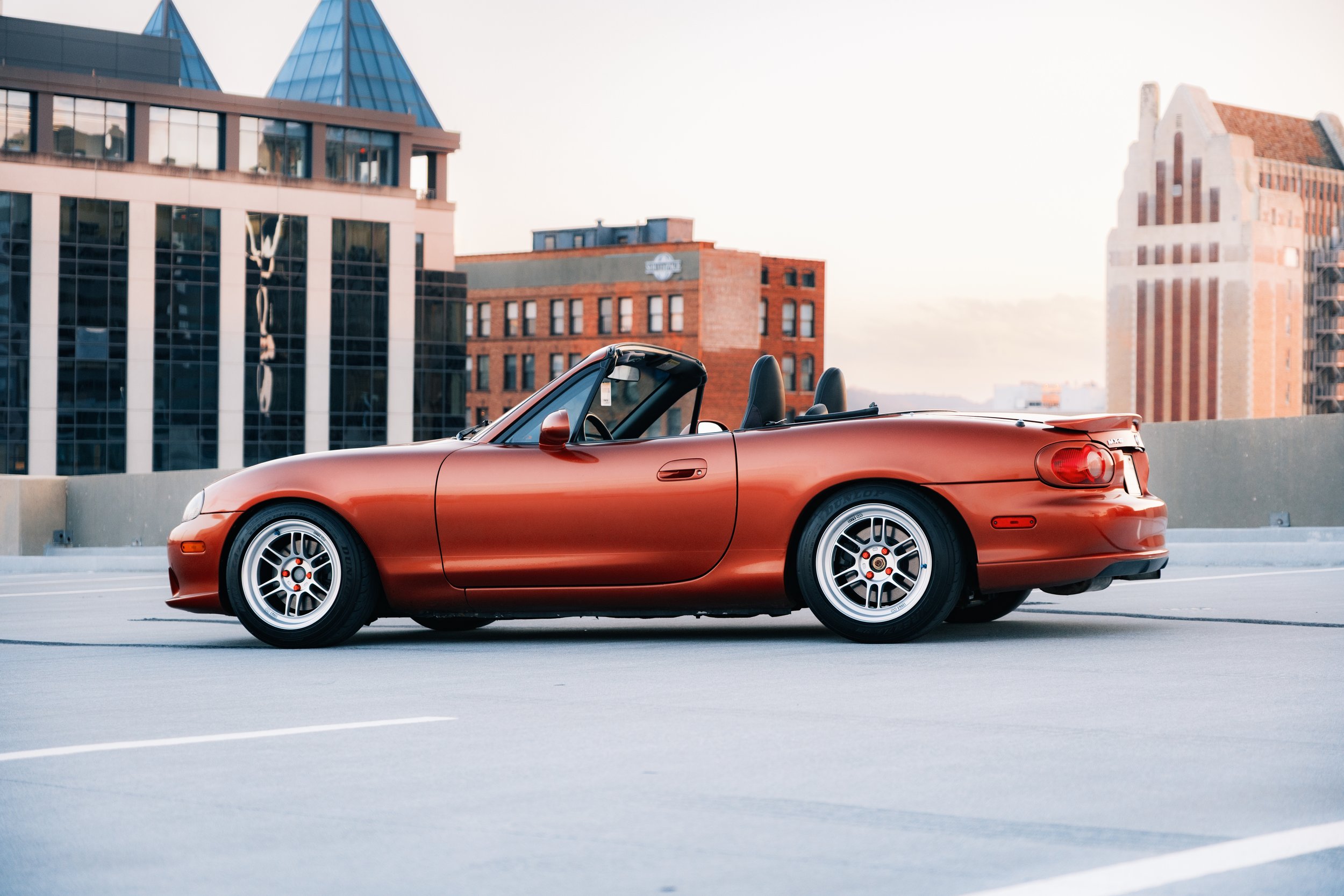 A red convertible sports car parked on a rooftop parking garage with a city skyline in the background.