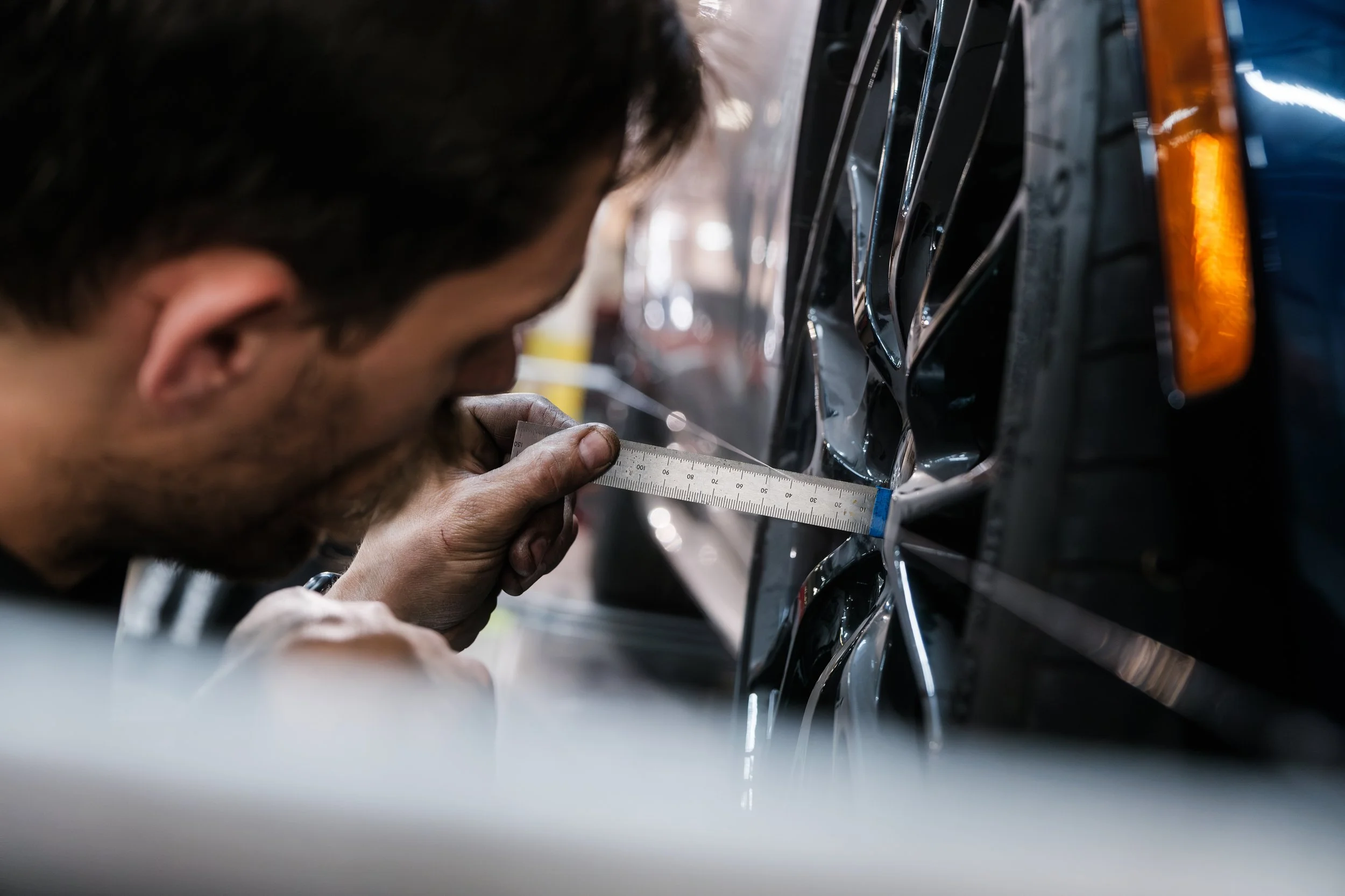 A man inspecting the wheel of a car with a measuring tool.