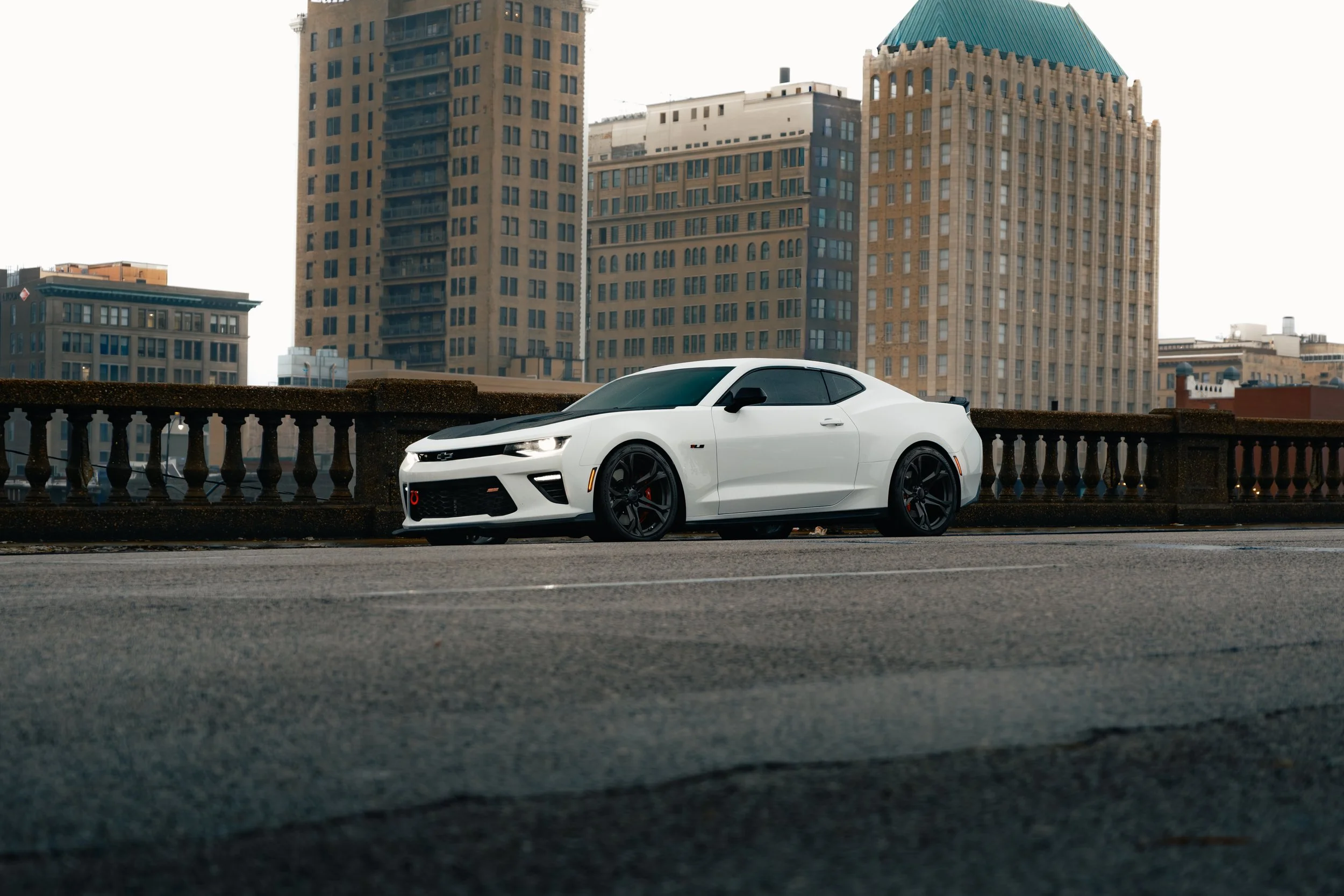 A white sports car parked on an urban street with high-rise buildings in the background.