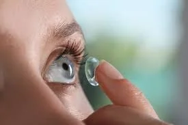 Person inserting contact lens into their eye.