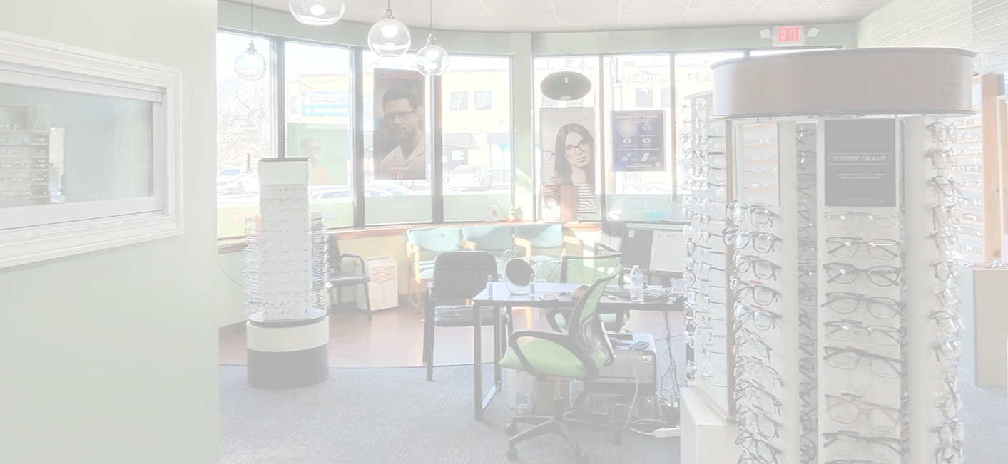 Interior of an optometry office with eye glasses display, a check-in desk, seating area with chairs, and posters in the windows.