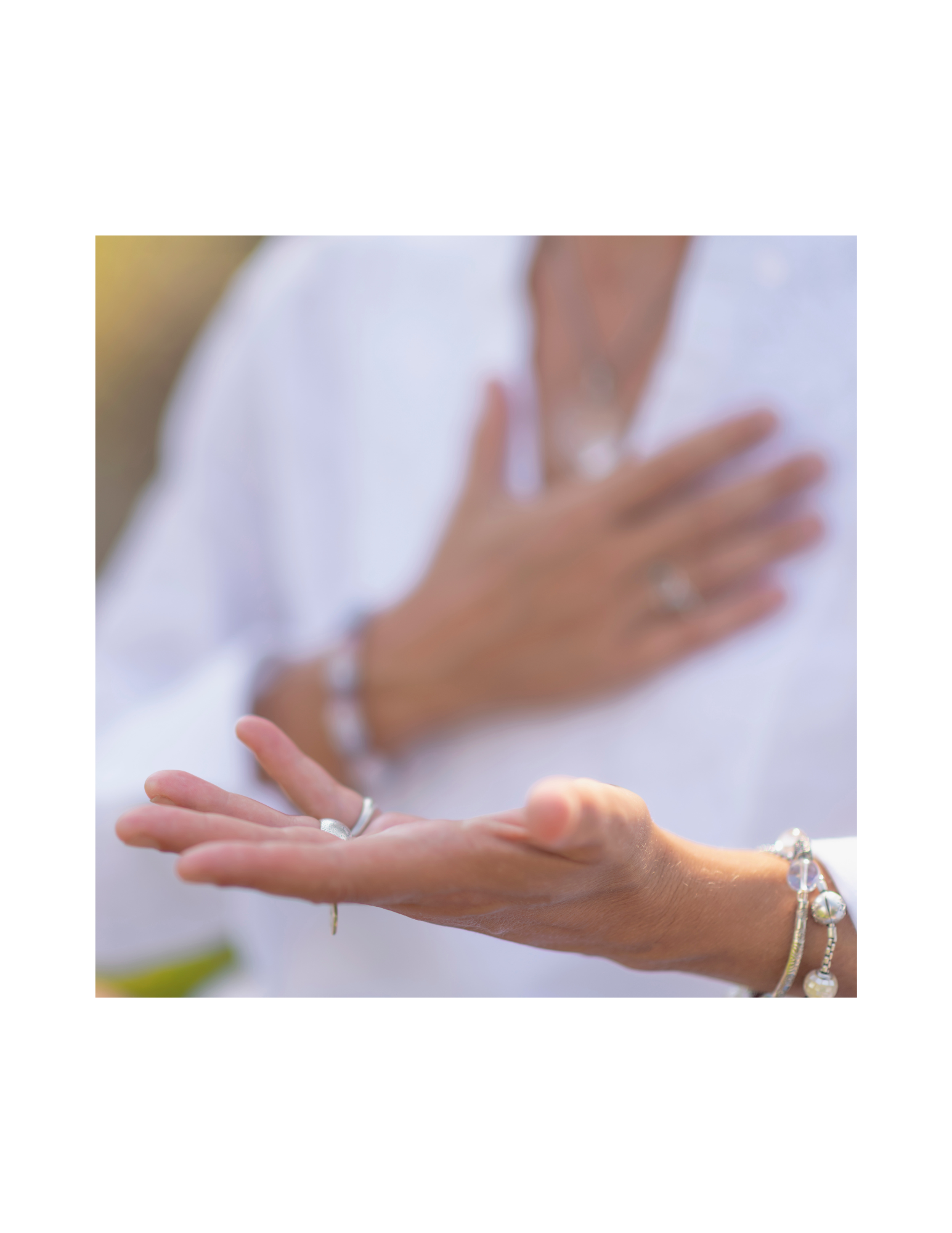 Close-up of a woman's hands with rings and bracelets, one hand on her chest and the other extended outward.