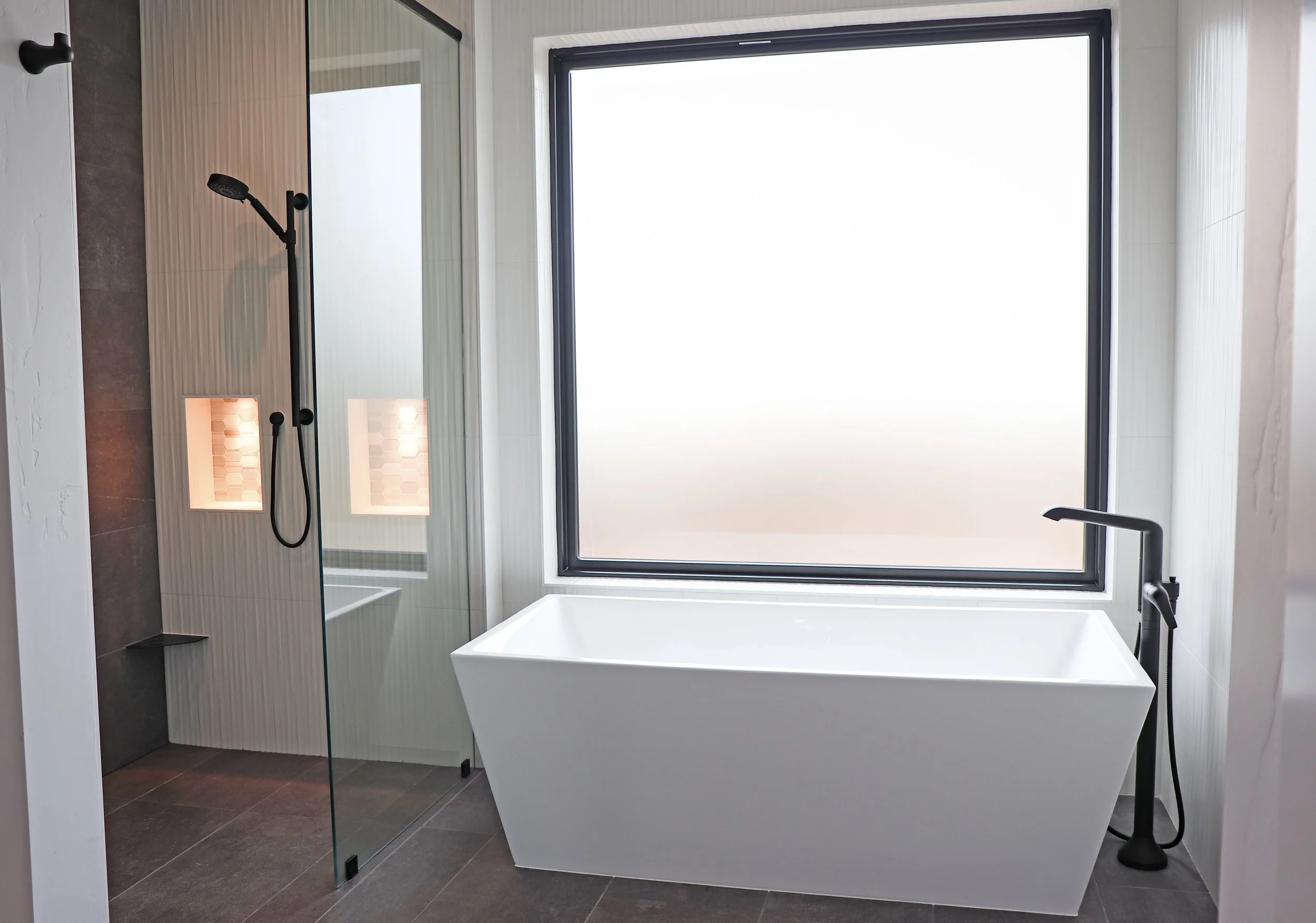 Modern bathroom with a freestanding bathtub next to a large frosted window, with a walk-in shower with a glass door and black fixtures.