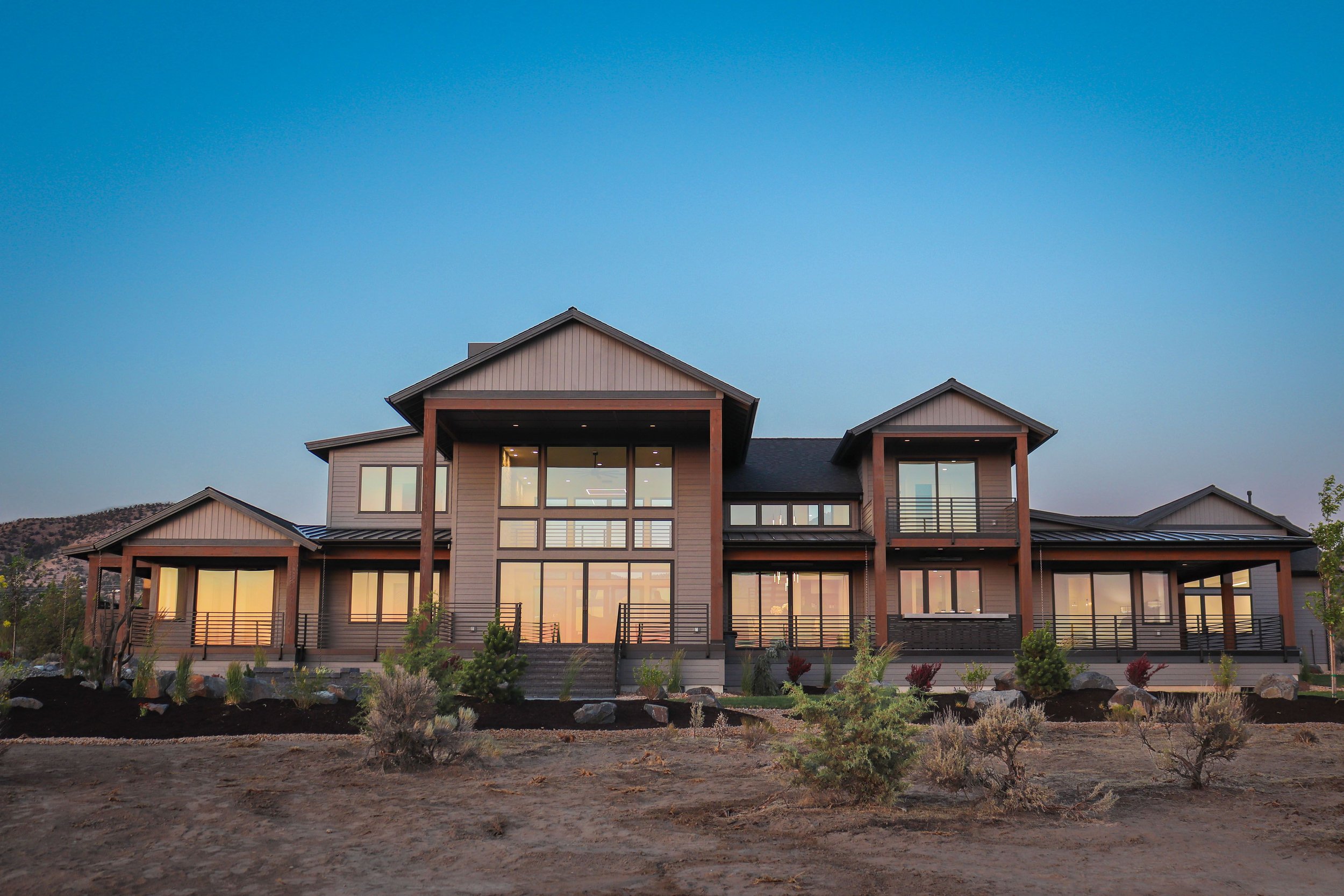 Modern house with large windows, balconies, and a multi-level design, set against a clear sky and a desert landscape.