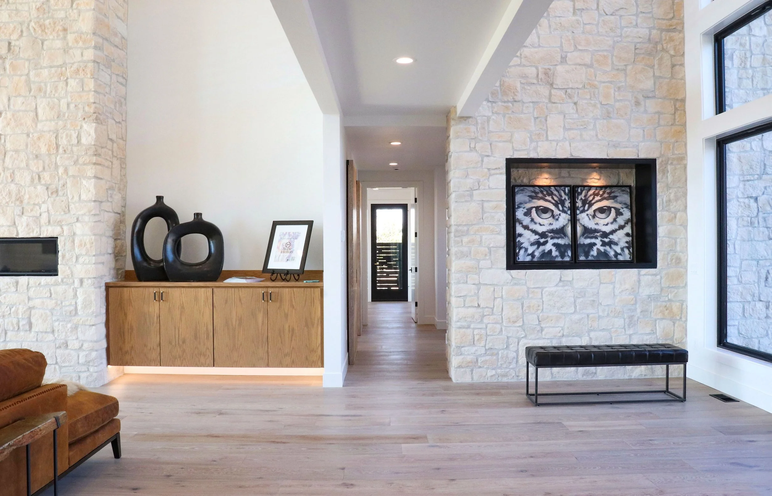 Modern interior living room with stone fireplace, bench, and hallway leading to the door.
