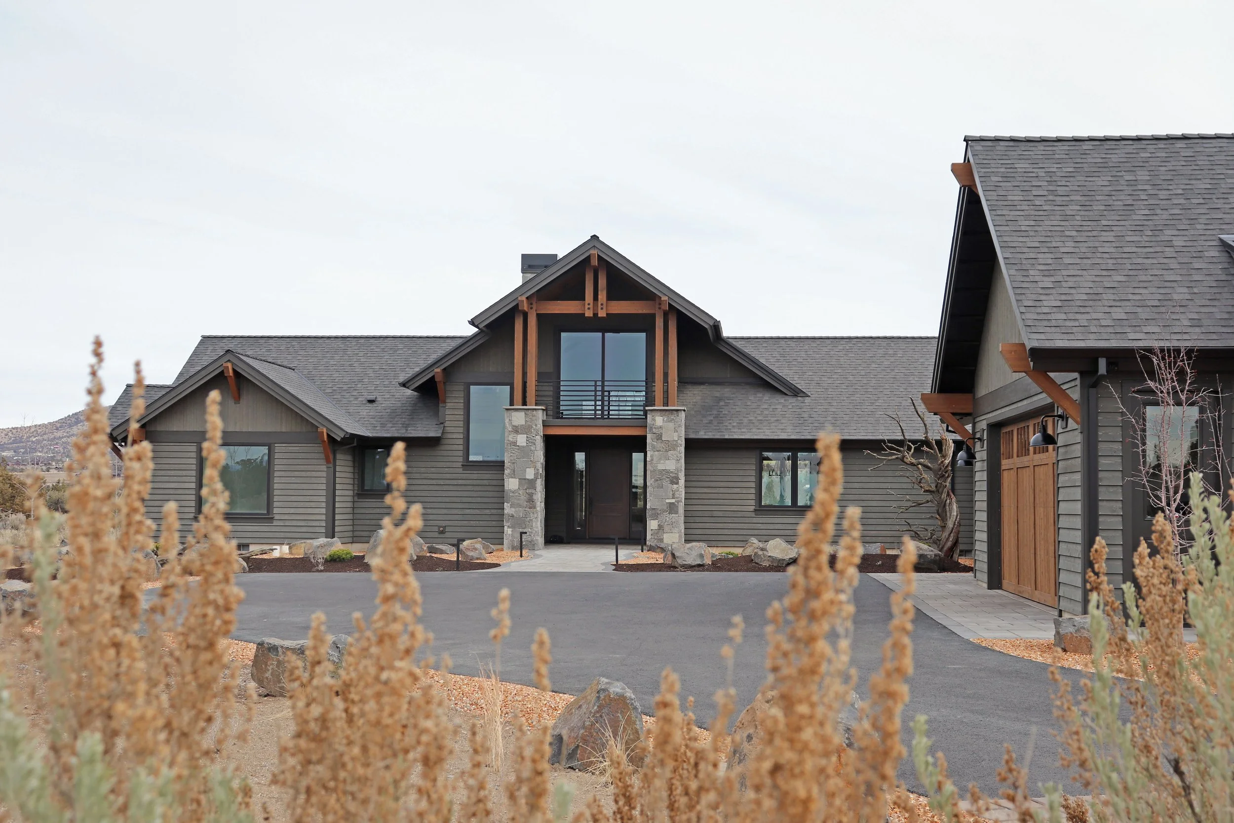 Modern house with gray siding, stone accents, and a sloped roof, surrounded by desert plants and rocks.
