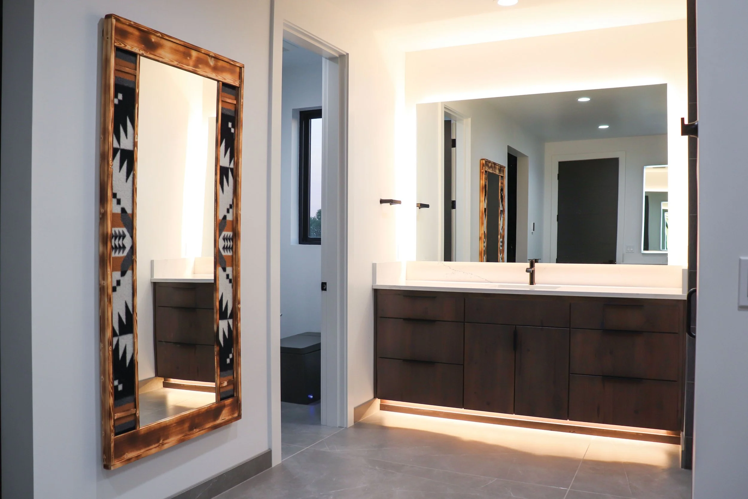 Modern bathroom with large mirror, wooden vanity, white countertop, and a Navajo style wall mirror.