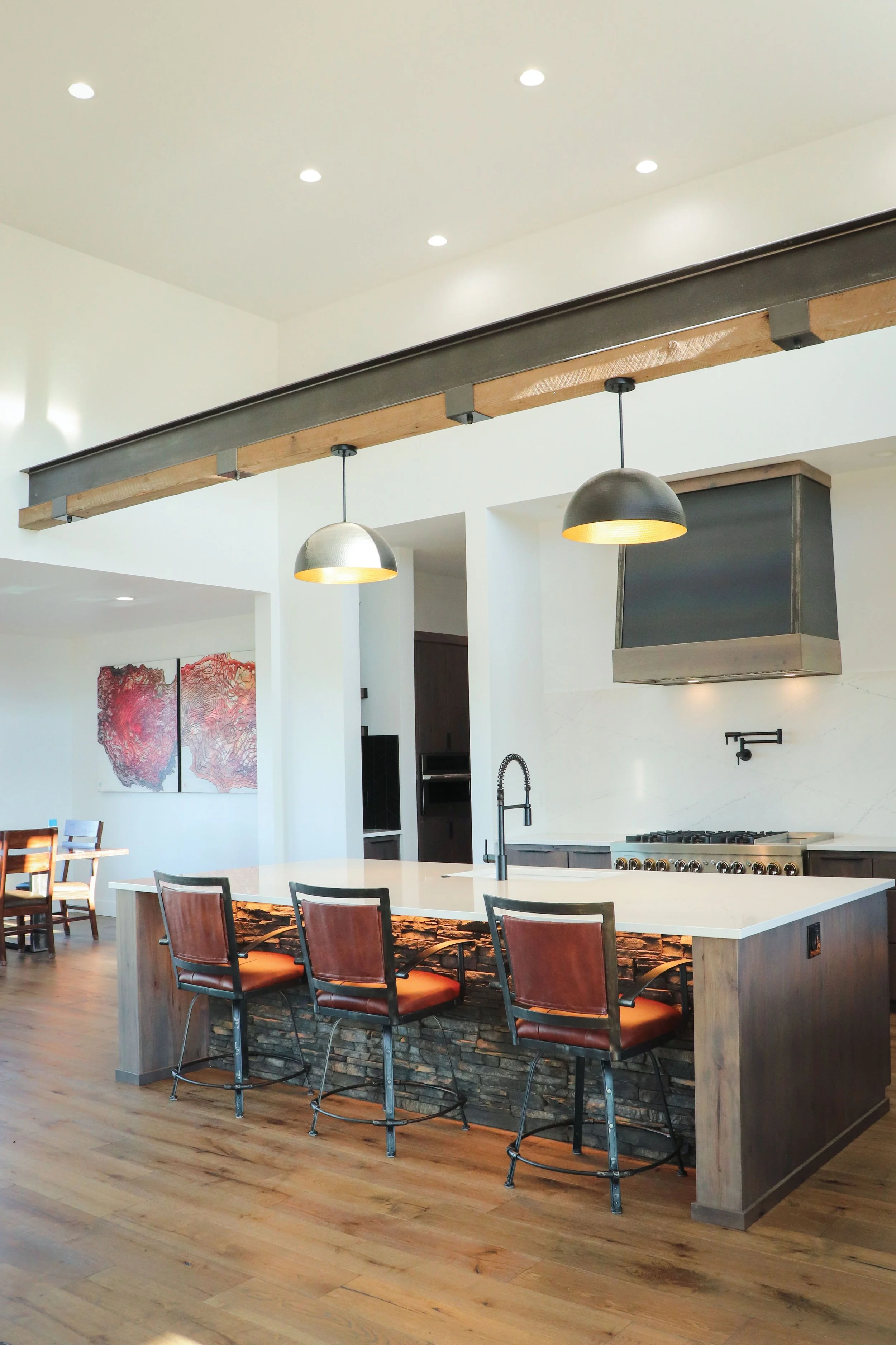 Modern kitchen with a large white island, three barstools, a stove with a range hood, pendant lighting, and wooden flooring.