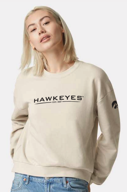 Young woman with blonde hair wearing a cream-colored sweatshirt with 'HAWKEYES' logo and jeans.