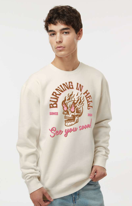 Young man wearing a white sweatshirt with a flaming skull graphic and pink text that says 'Burning in Hell' and 'See you soon!'