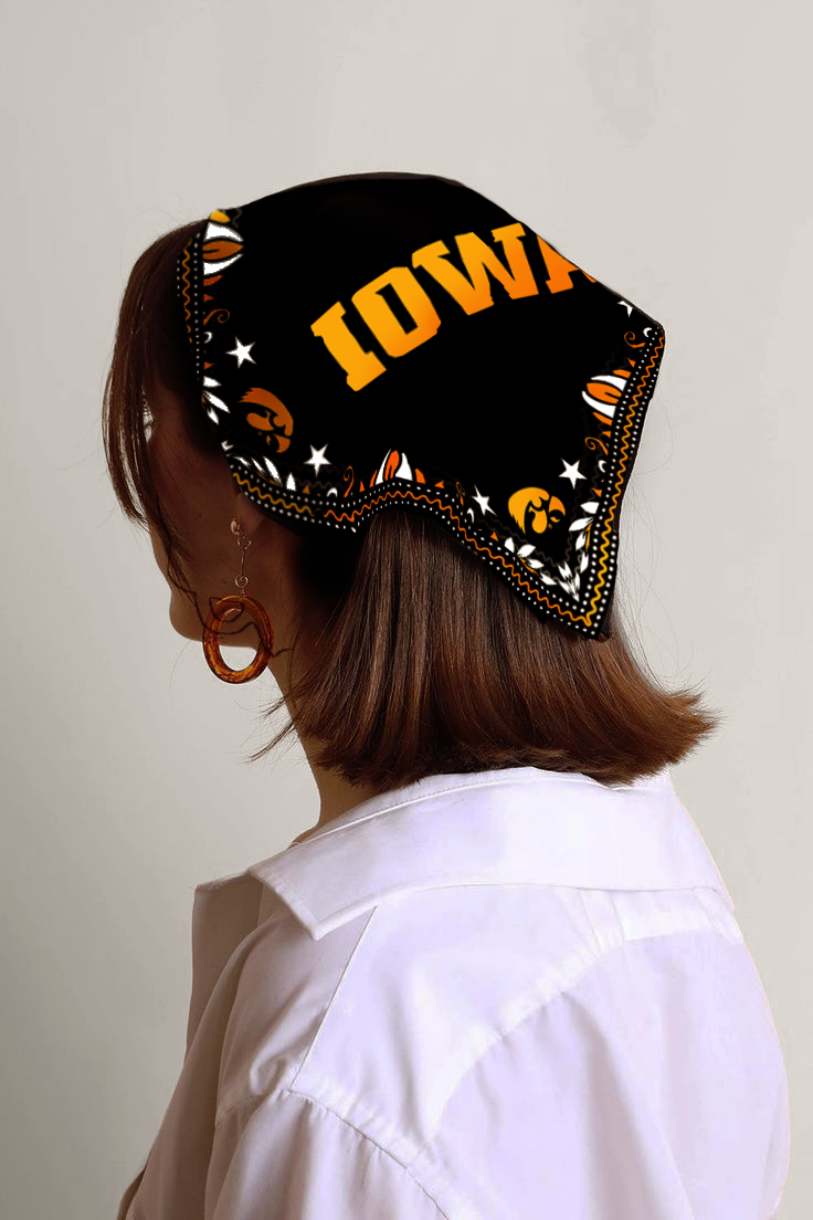 Woman with brown hair wearing a black bandana with orange and white patterns and letters, and large orange earrings, dressed in a white shirt.