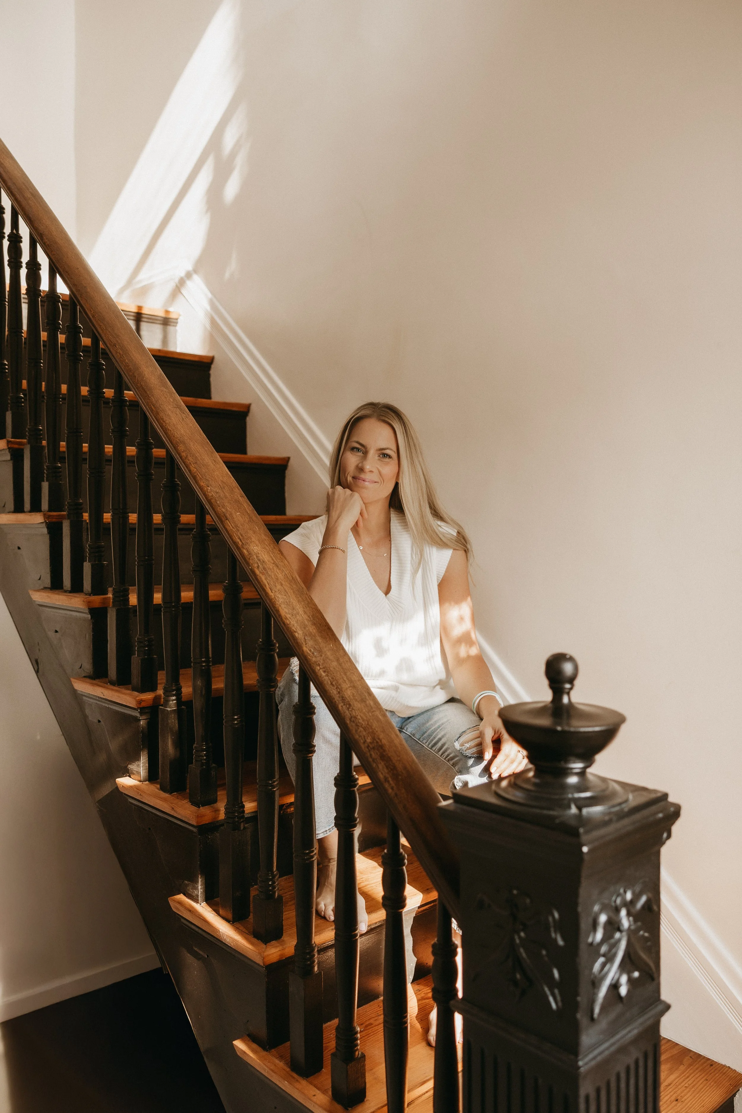 Founder of femwell, Allie Janszen, sitting on wooden stairs with black spindles, smiling and resting her chin on her hand.