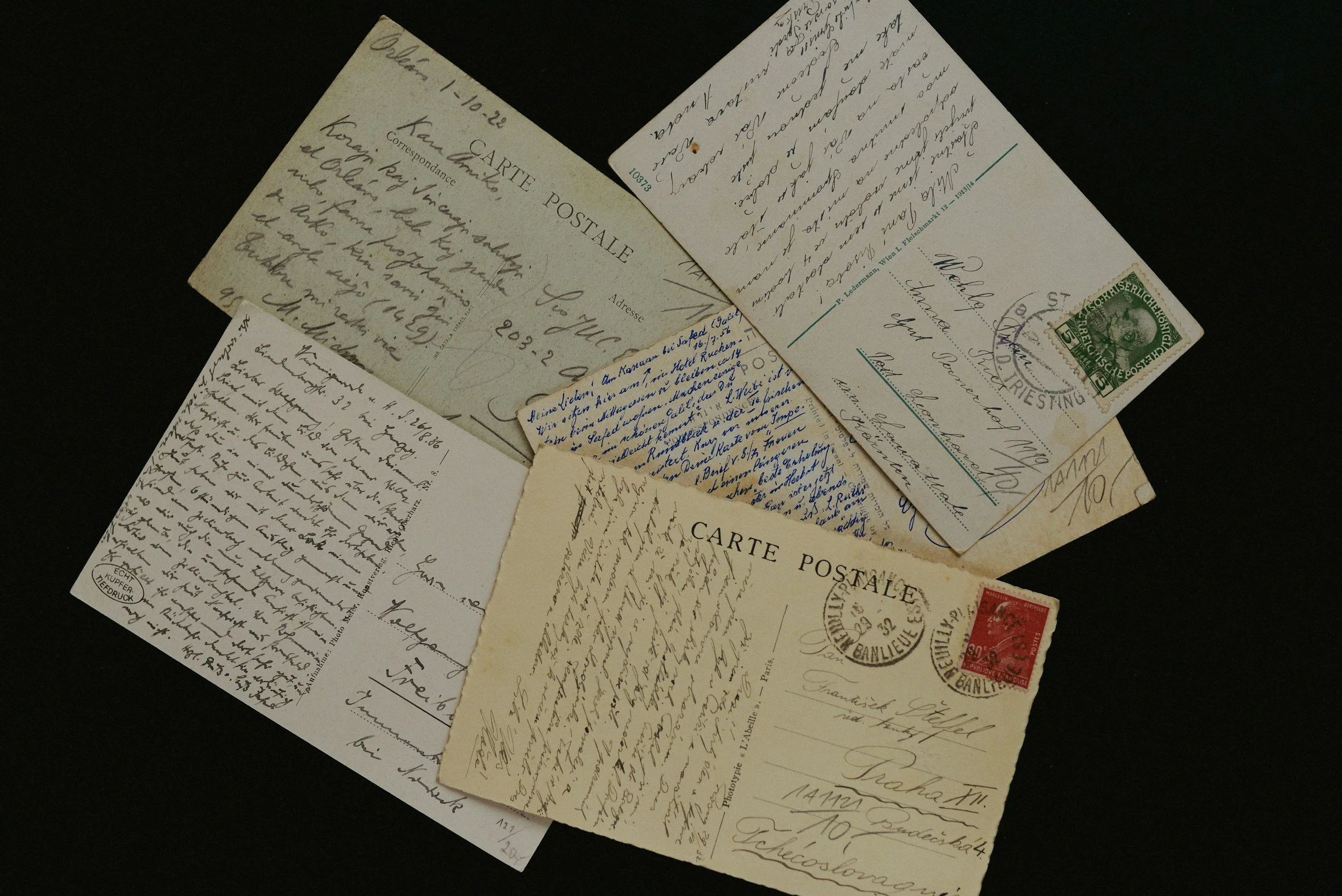 Collection of vintage postcards with handwritten messages and postage stamps, overlapping each other on a black surface.